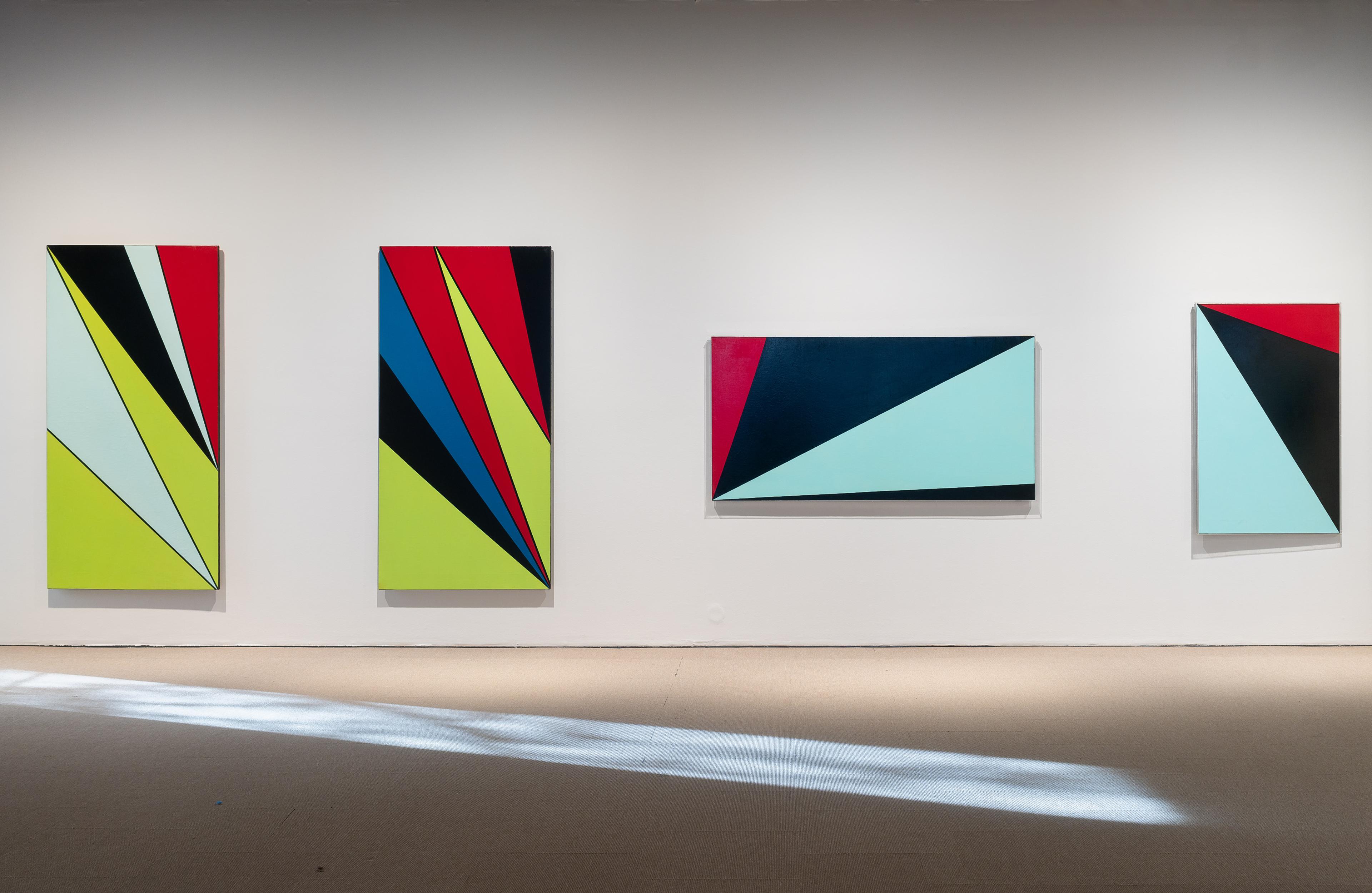 Vi ser tre abstrakte malerier i flere farger, på en hvit utstillingsvegg
