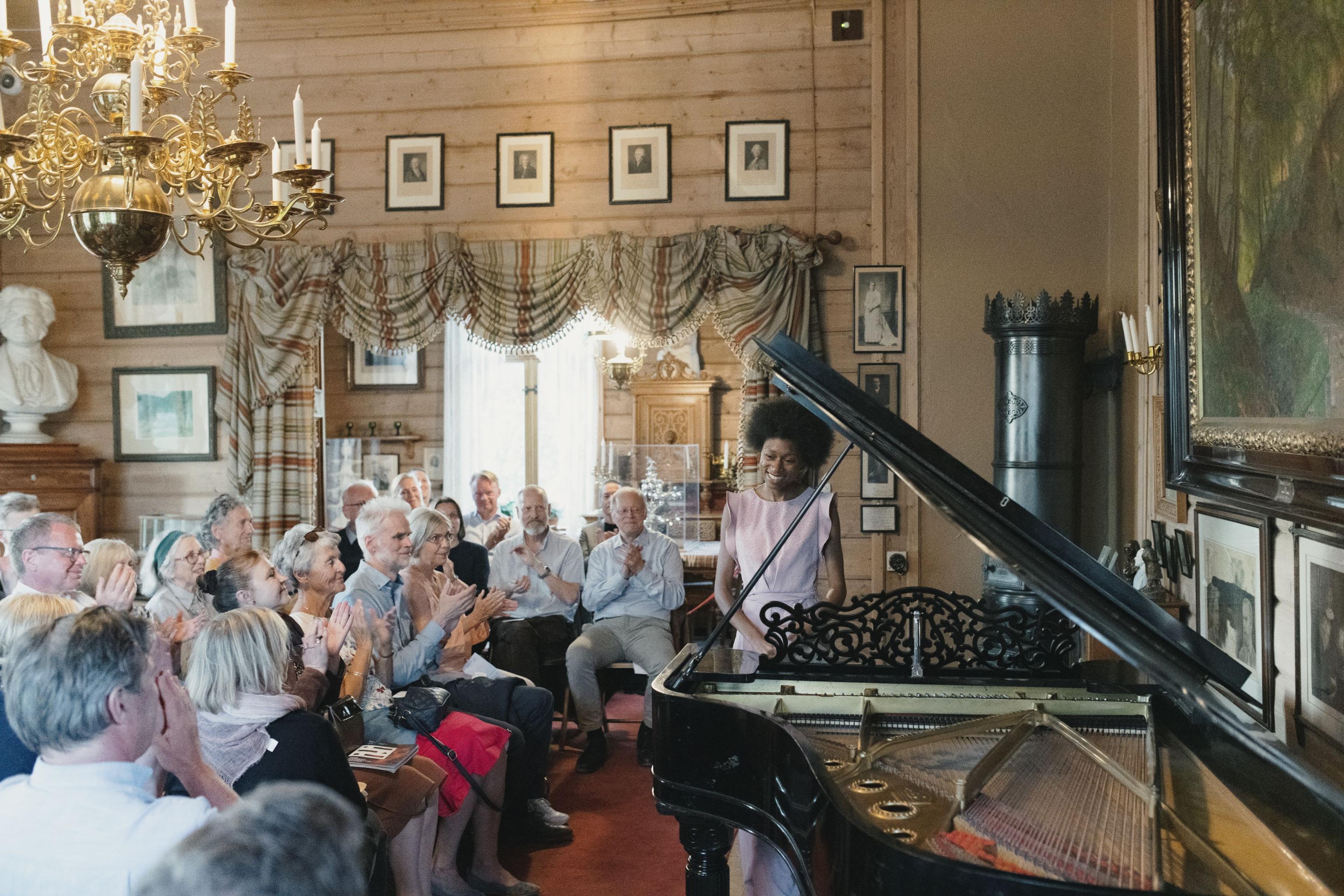 En gruppe publikummere i Griegs villa gir applaus til en pianist. Hun smiler og står ved flygelet.