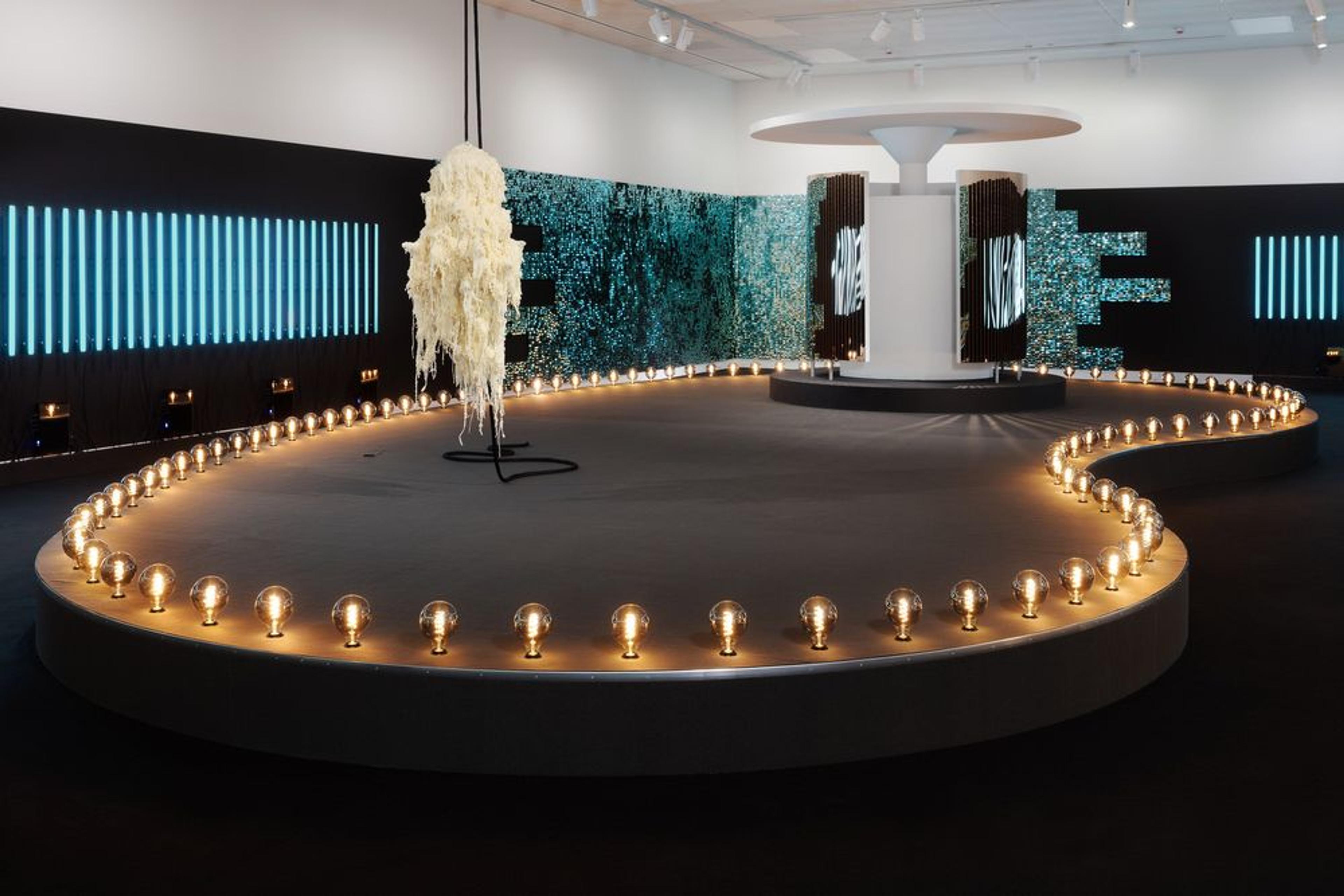 En installasjon av Børre Sæthre, som framstiller et hvitt urinal, plassert oppå en oval scenestruktur, med glødende lyspærer.