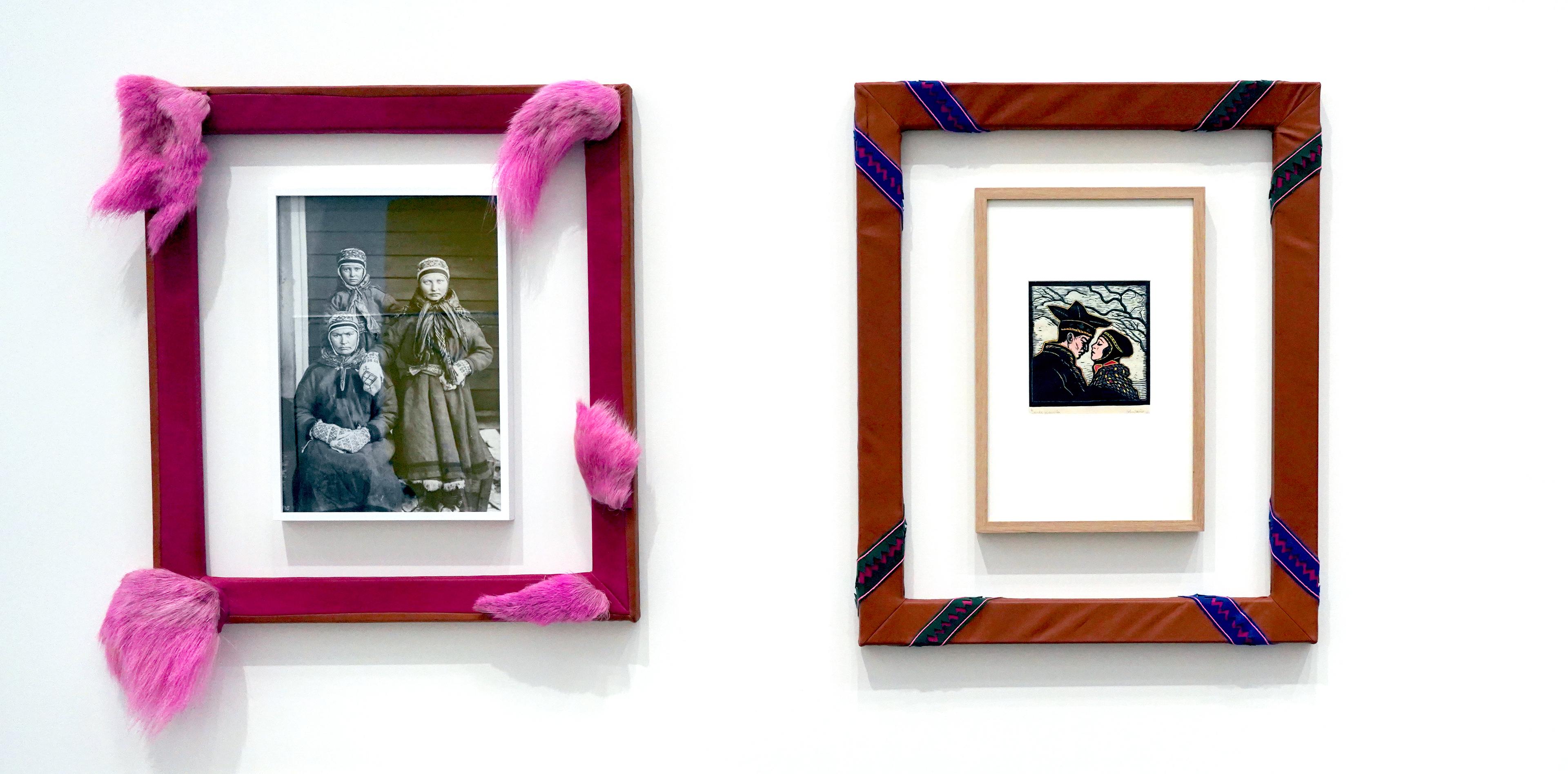 Foto av to kunstverk på vegg, ett fotografi av en gruppe samiske kvinner i sort-hvitt omgitt av en rosa ramme i reinskinn og pels, og et lite trykk av et koftekledt par som kysser, omgitt av en ramme utført i duodji-teknikk. 