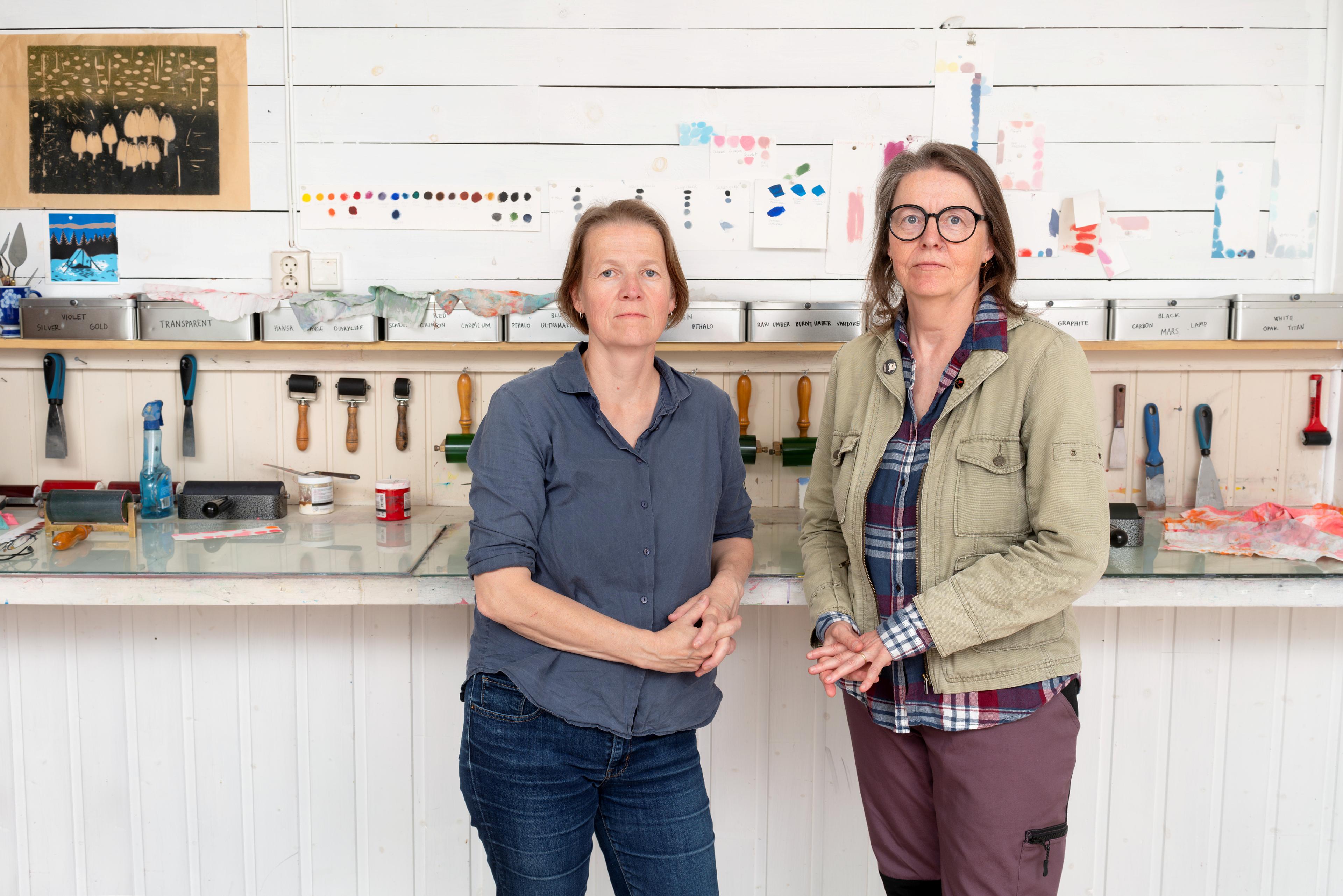 Portrait of the artists and sisters Caroline and Annette Kierulf, standing in a atelier room filled with graphic tools.