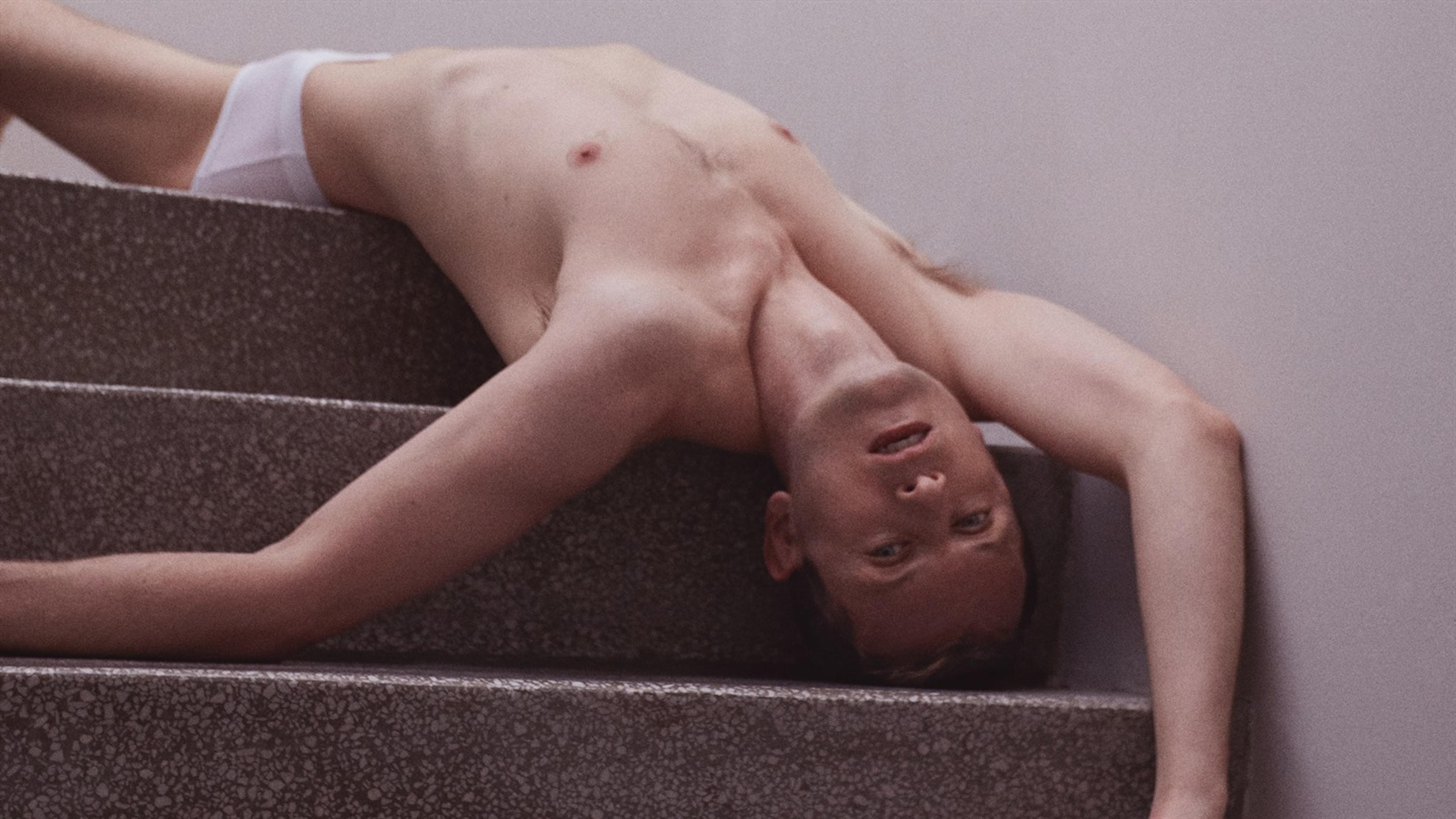 En mann ikledd hvit underbukse ligger på ryggen i en trapp