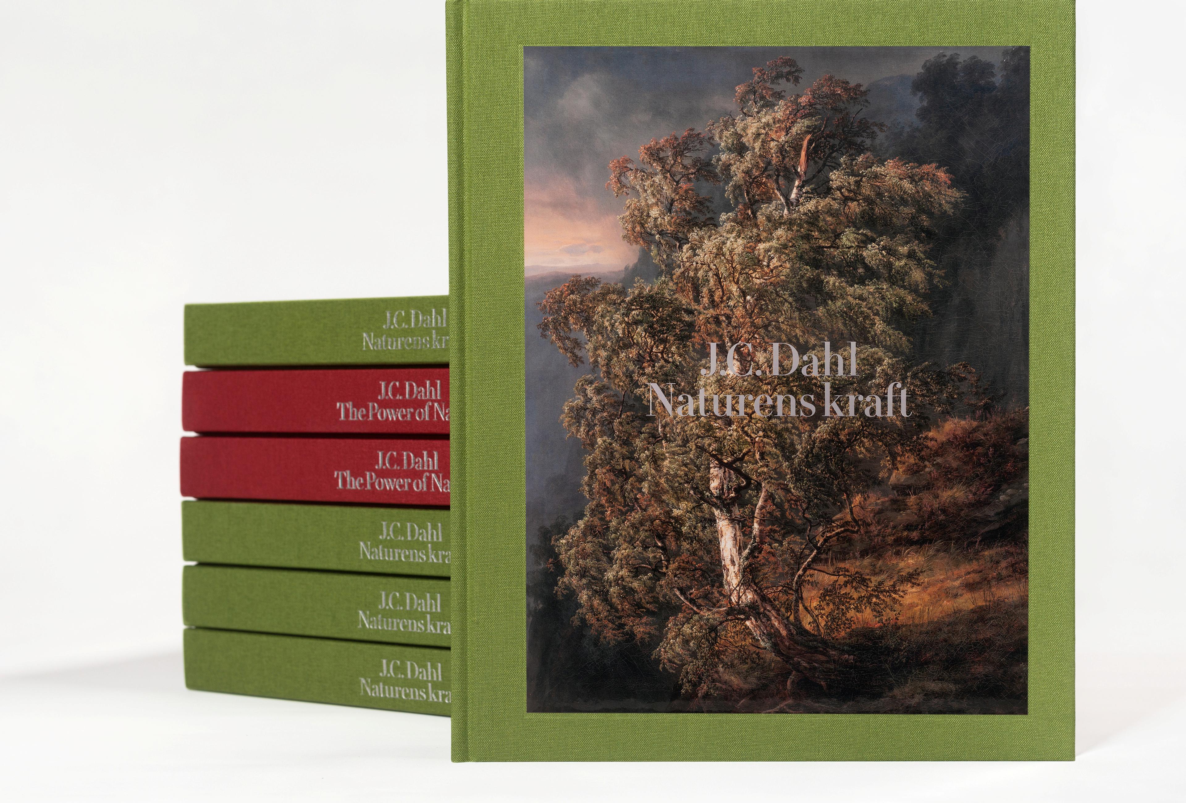 En katalog for utstillingen «J.C. Dahl. Naturens kraft» står foran en stabel med flere kataloger