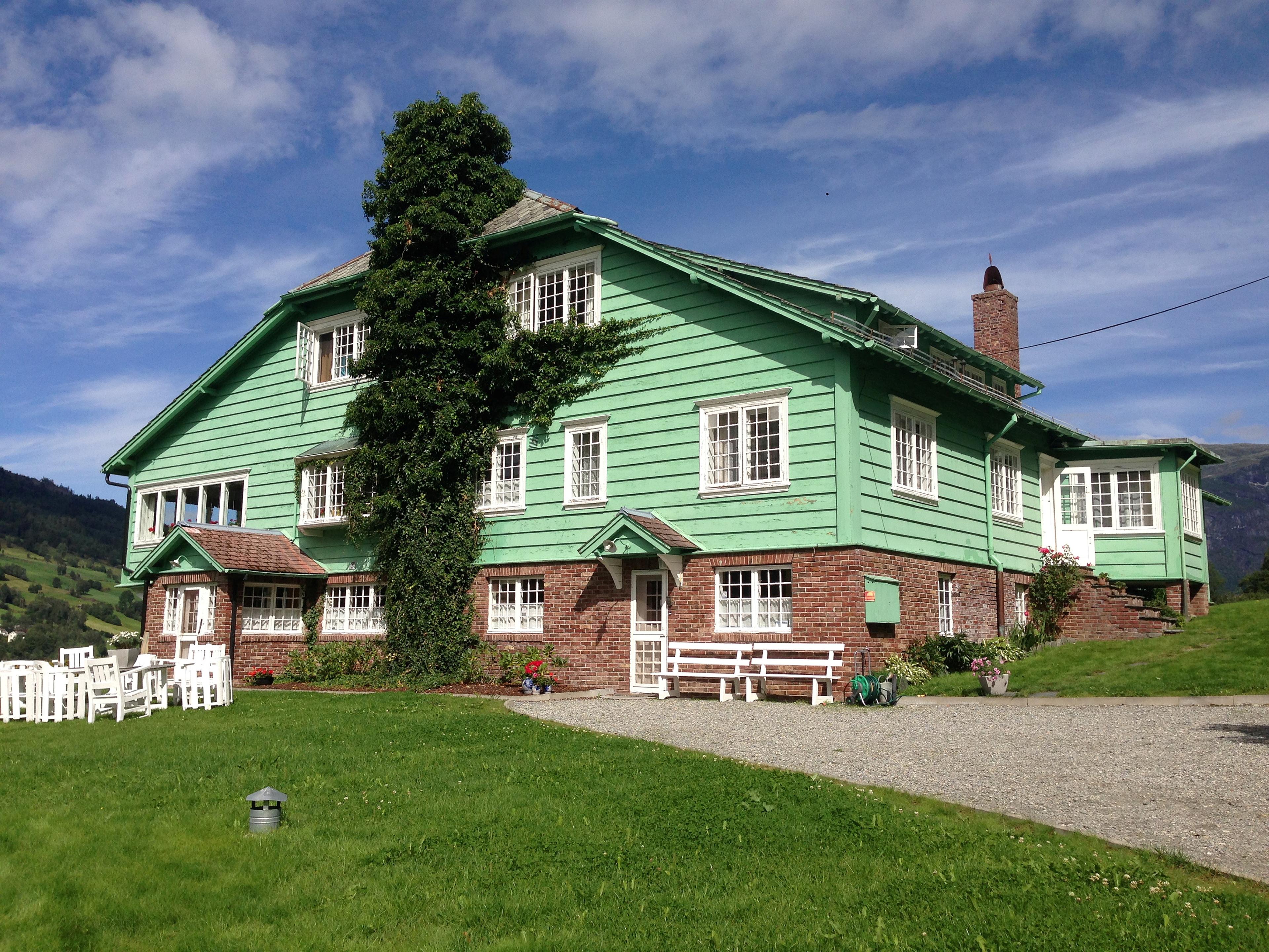 En grønnmalt villa med brun mur, i et sommerlig landskap i Olden.