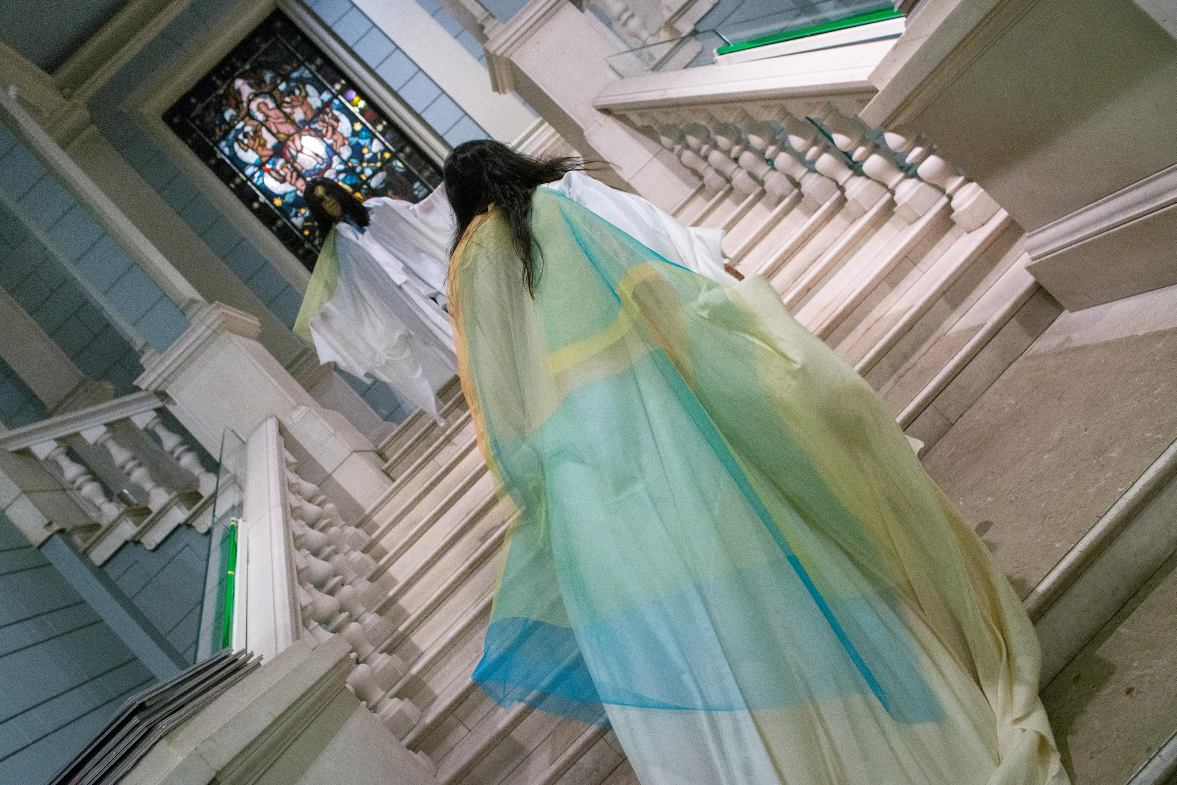 From a performance at Permanenten, with a person running up the stairs, with a colorful textile flowing behind them.