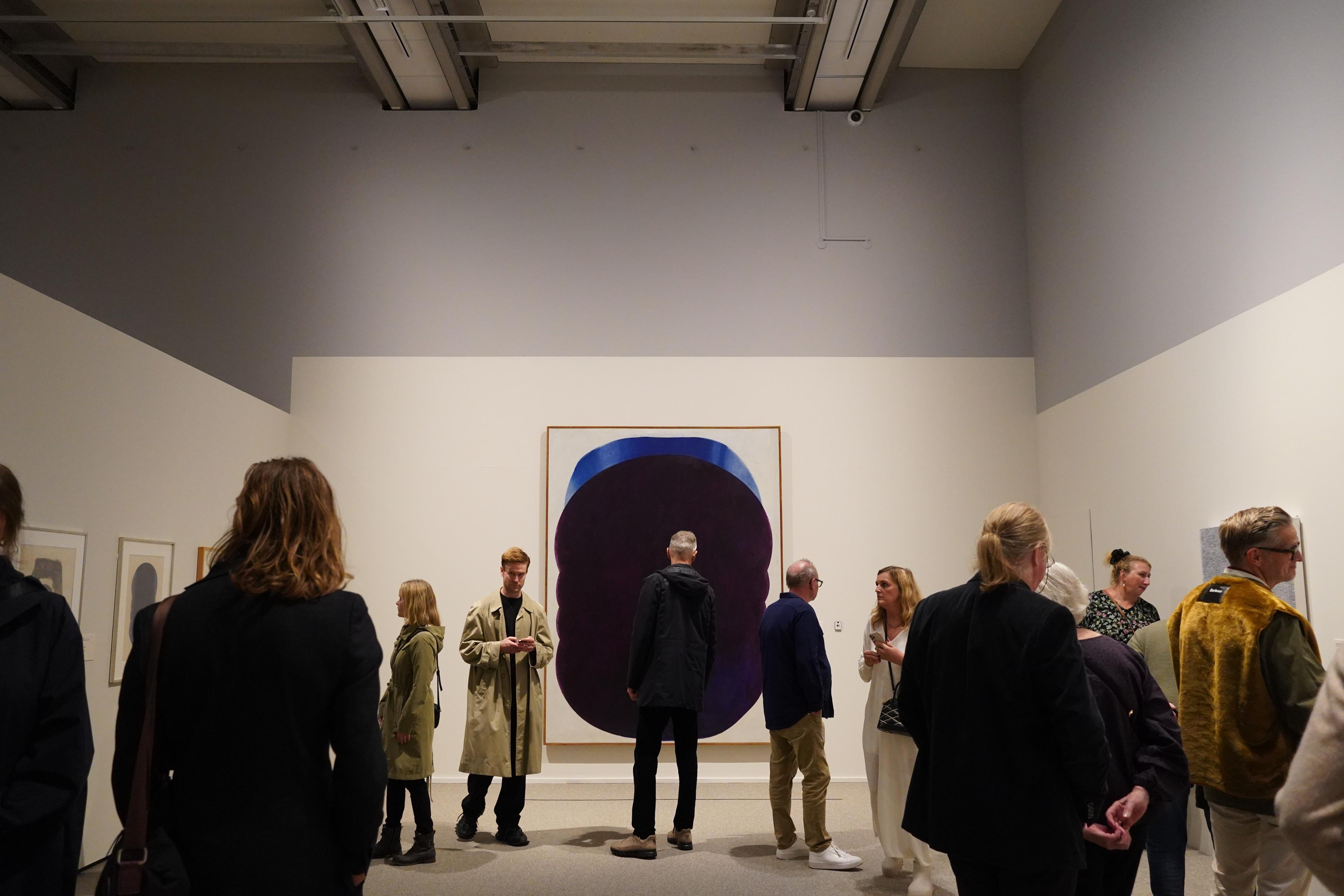 Flere personer står med ryggen til kamera, foran et abstrakt maleri, som henger på en hvit utstillingsvegg