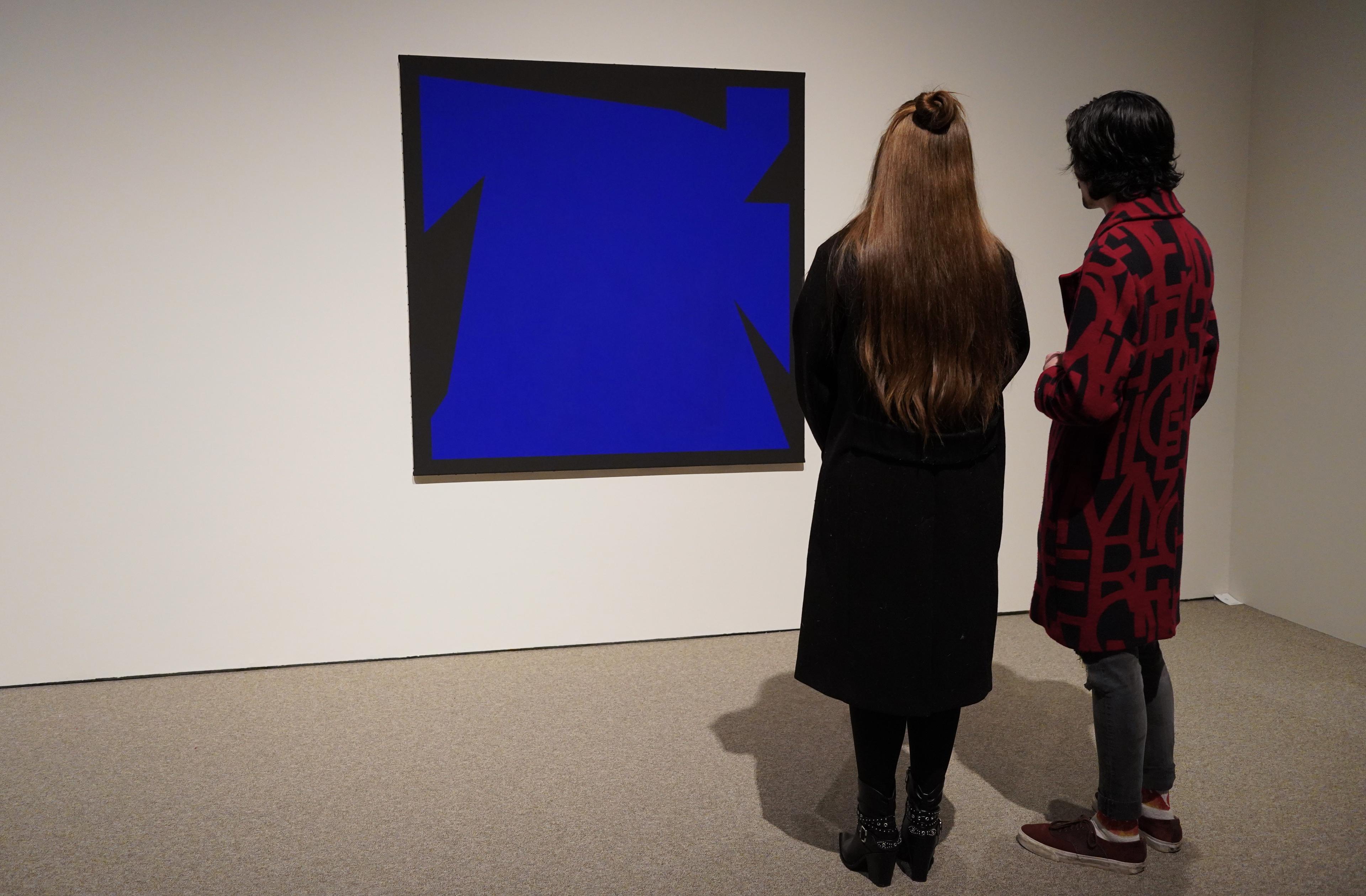 To personer står med ryggen til kamera, foran et abstrakt maleri, som henger på en hvit utstillingsvegg