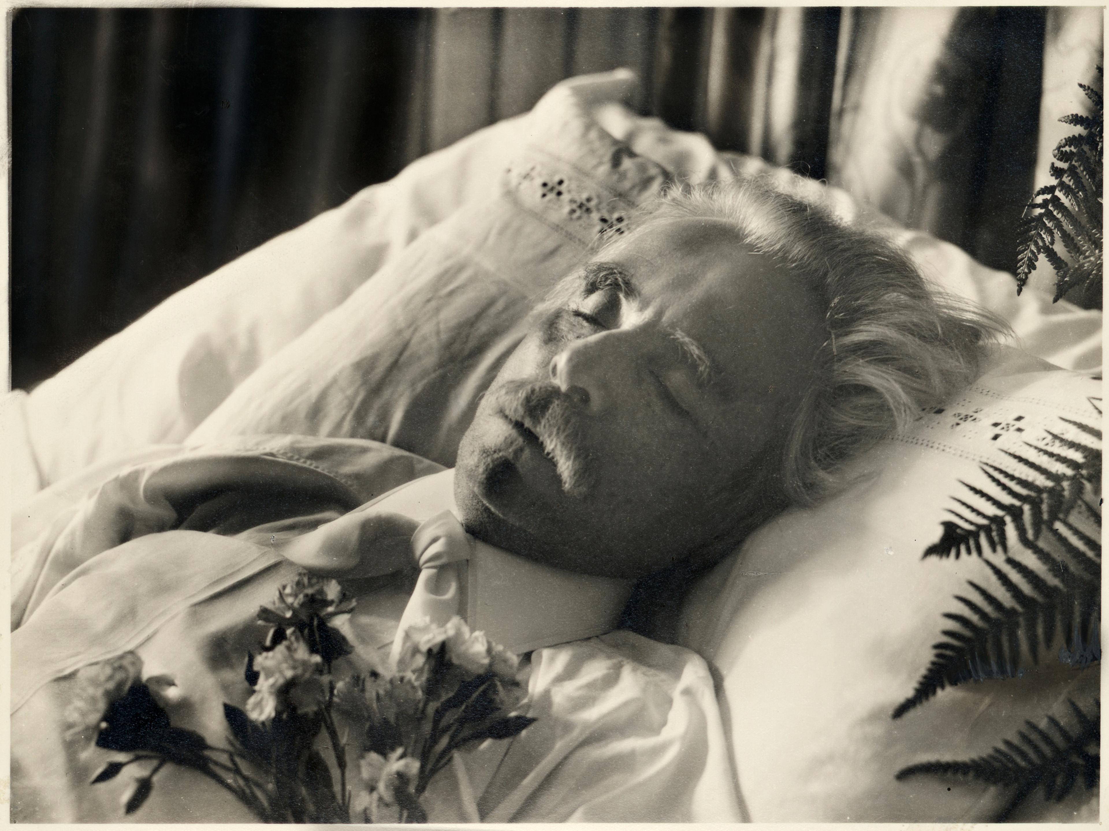 Sort-hvitt fotografi av den avdøde Edvard Grieg, som ligger på en seng med øynene lukket, på en hvit pute.