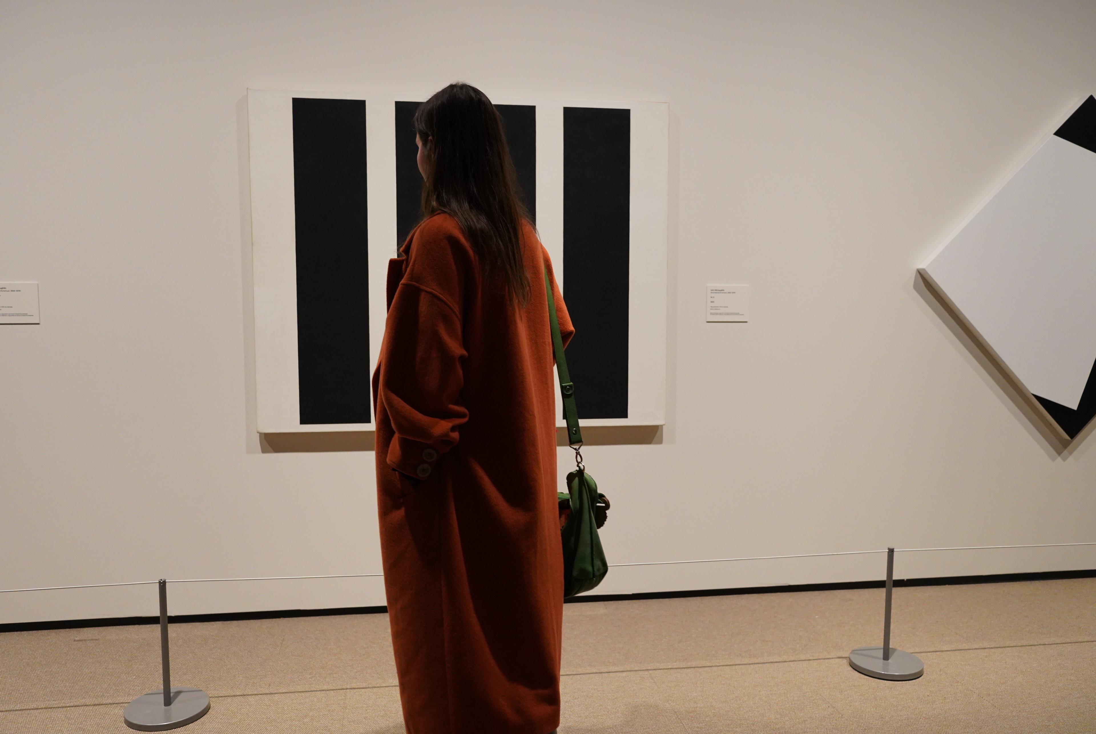 En person står med ryggen til kamera, foran et abstrakt maleri, som henger på en hvit utstillingsvegg