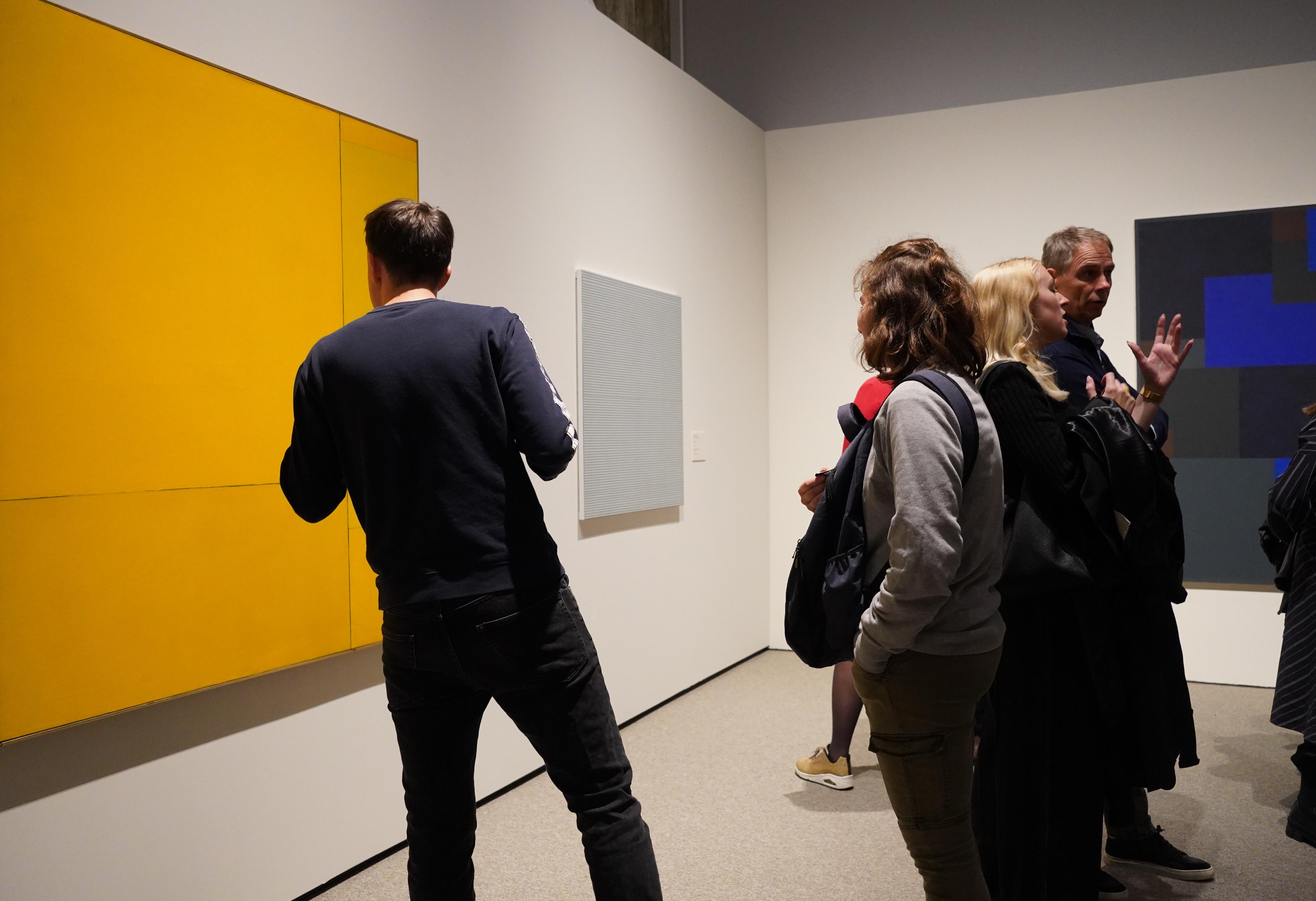 En person står med ryggen til kamera, foran et abstrakt maleri, som henger på en hvit utstillingsvegg