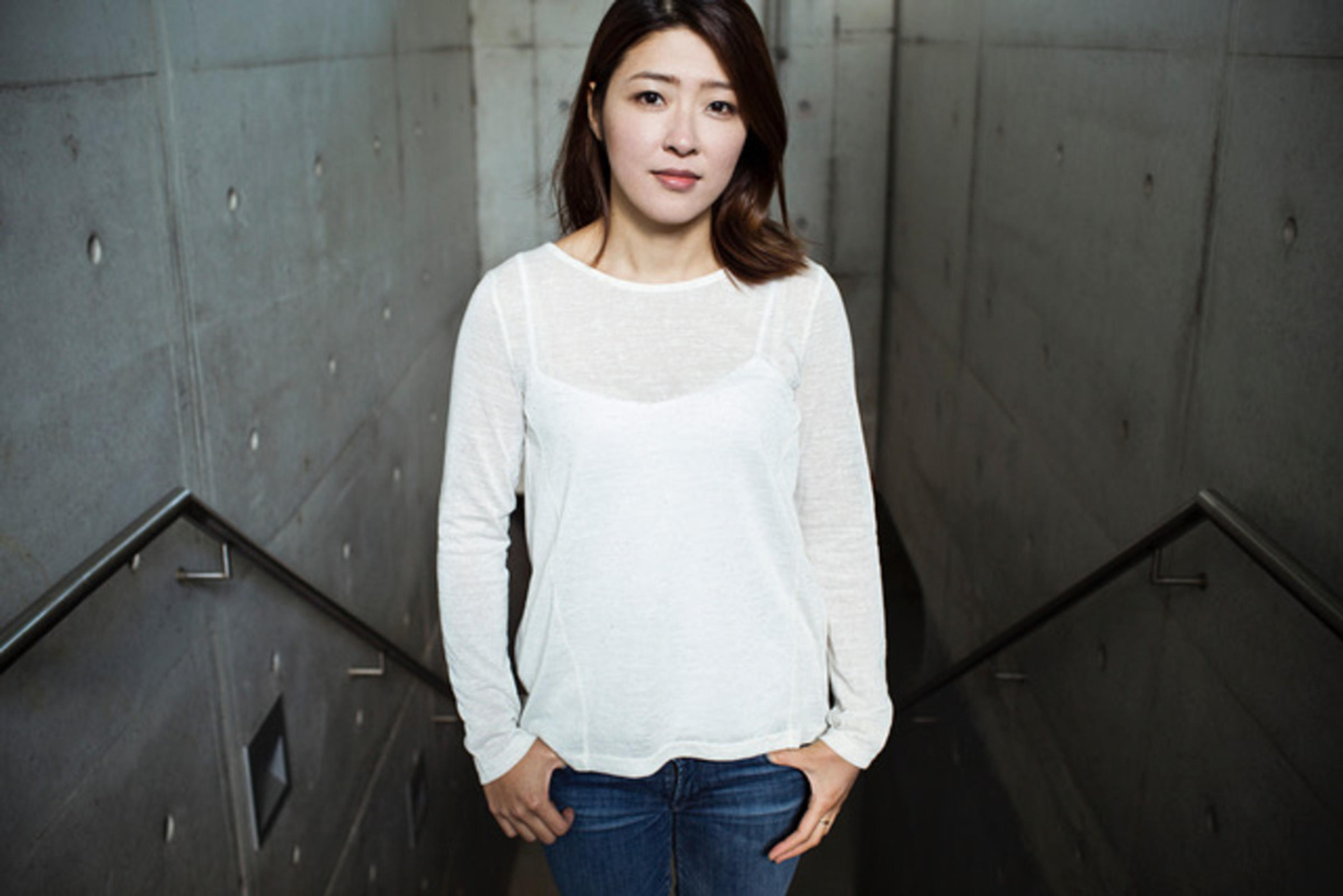 Foto av kvinne i jeans og hvit genser, stående i en grå trappeoppgang