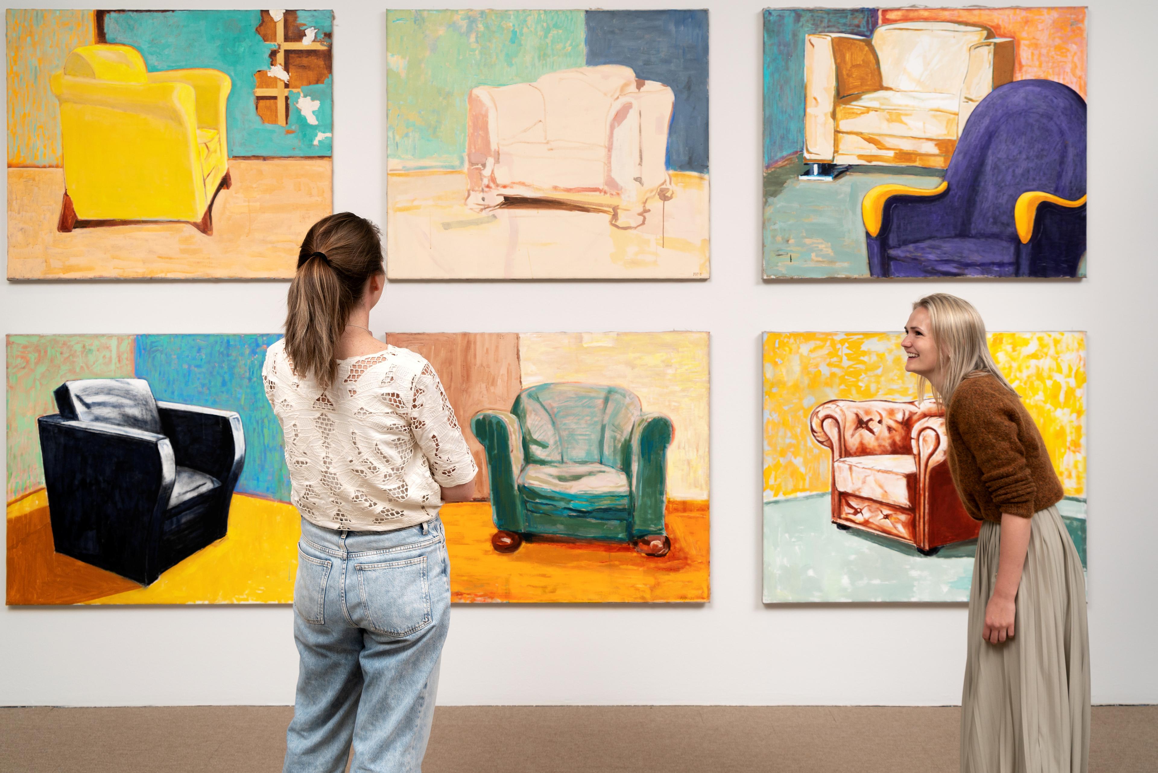 Foto av to kvinner som står foran noen store malerier på vegg og ler mot hverandre.