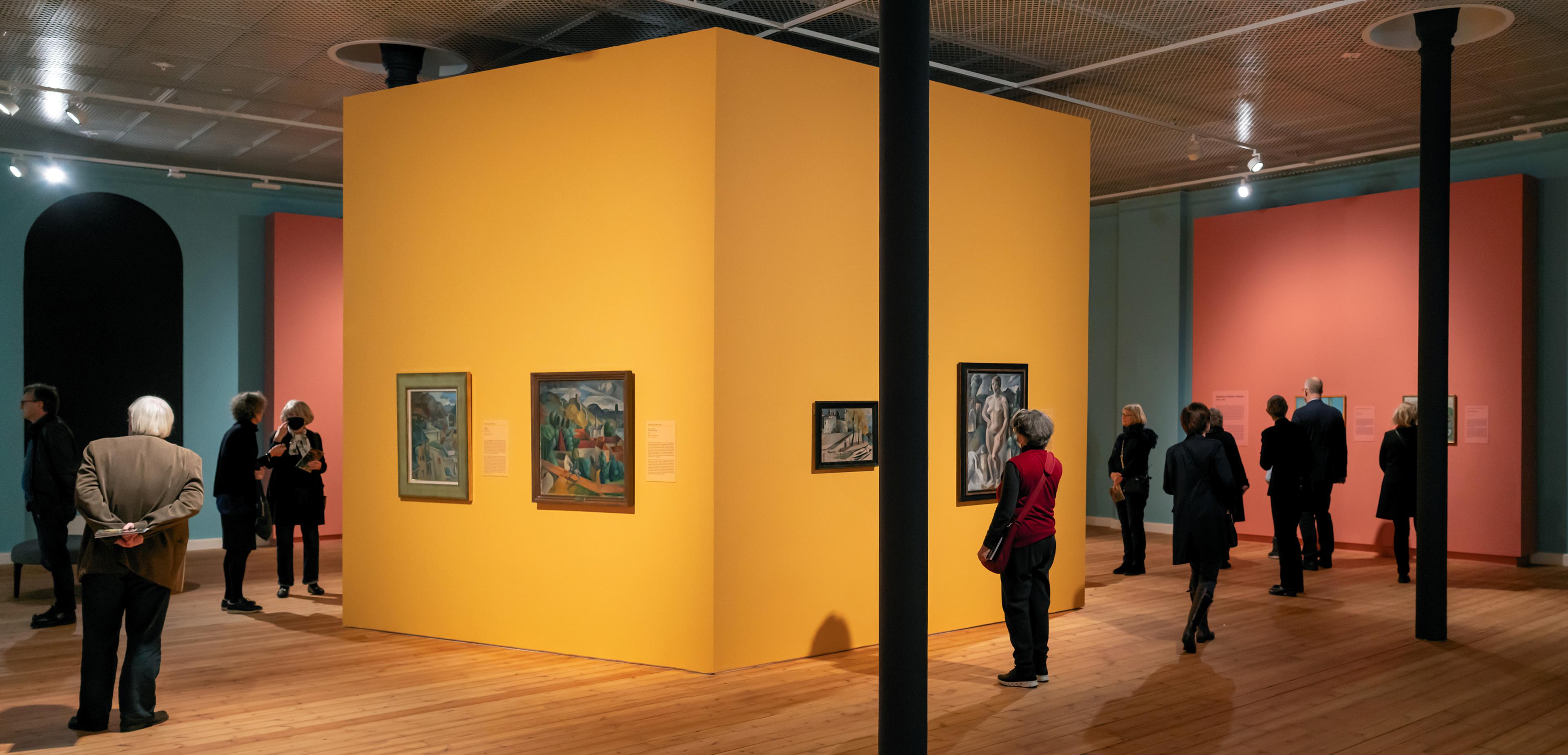 Et utstillingsrom i Permanenten, med vegger i gult, rosa og blått, og malerier på veggene.