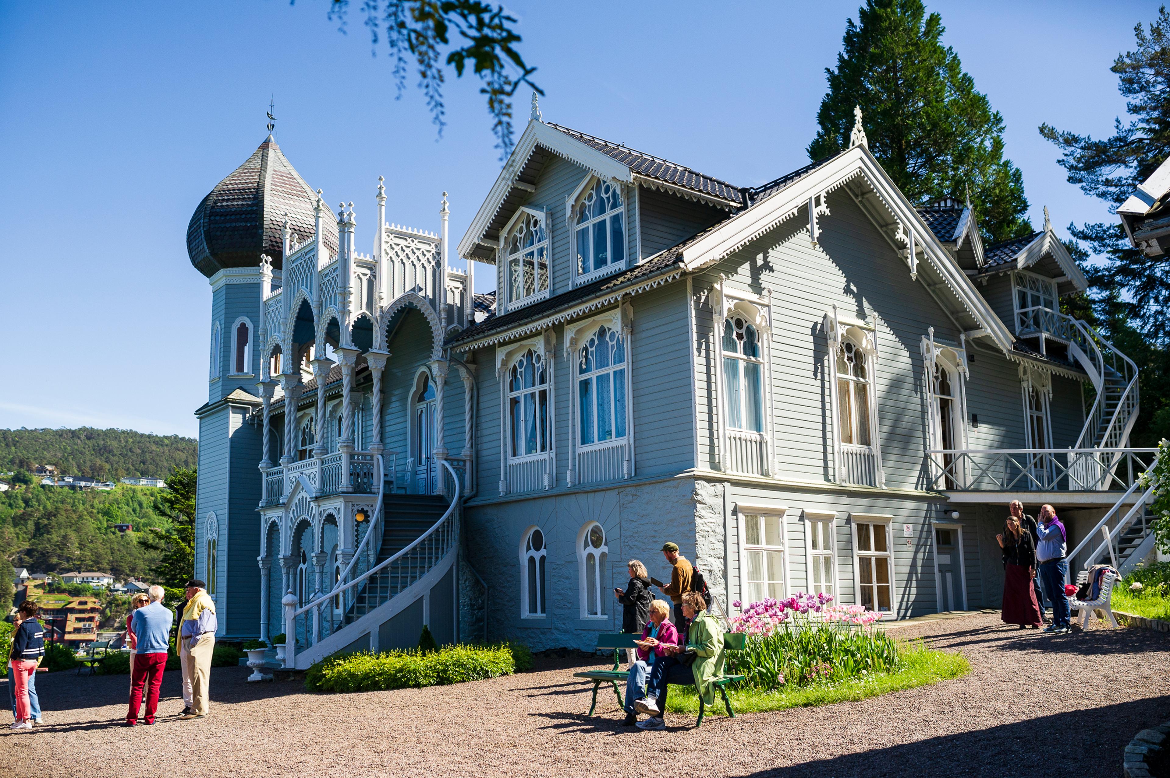 Villaen på Lysøen i sommersol, med flere personer på tunet utenfor.