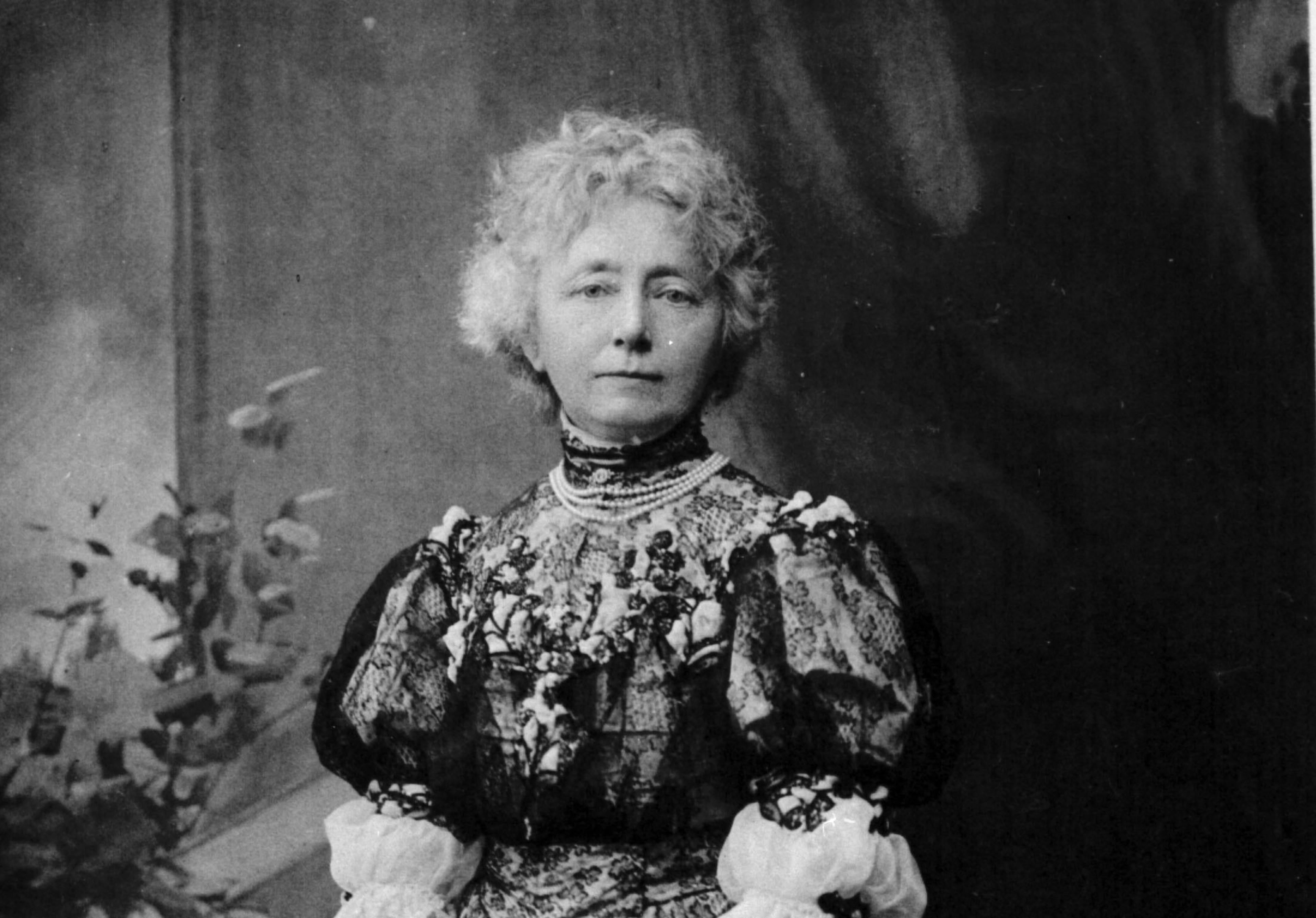 Et portrett av Nina Grieg i sort-hvitt, sett fra livet og opp. Hun ser i kamera, har en blondekjole. Oppsatt frisyre.
