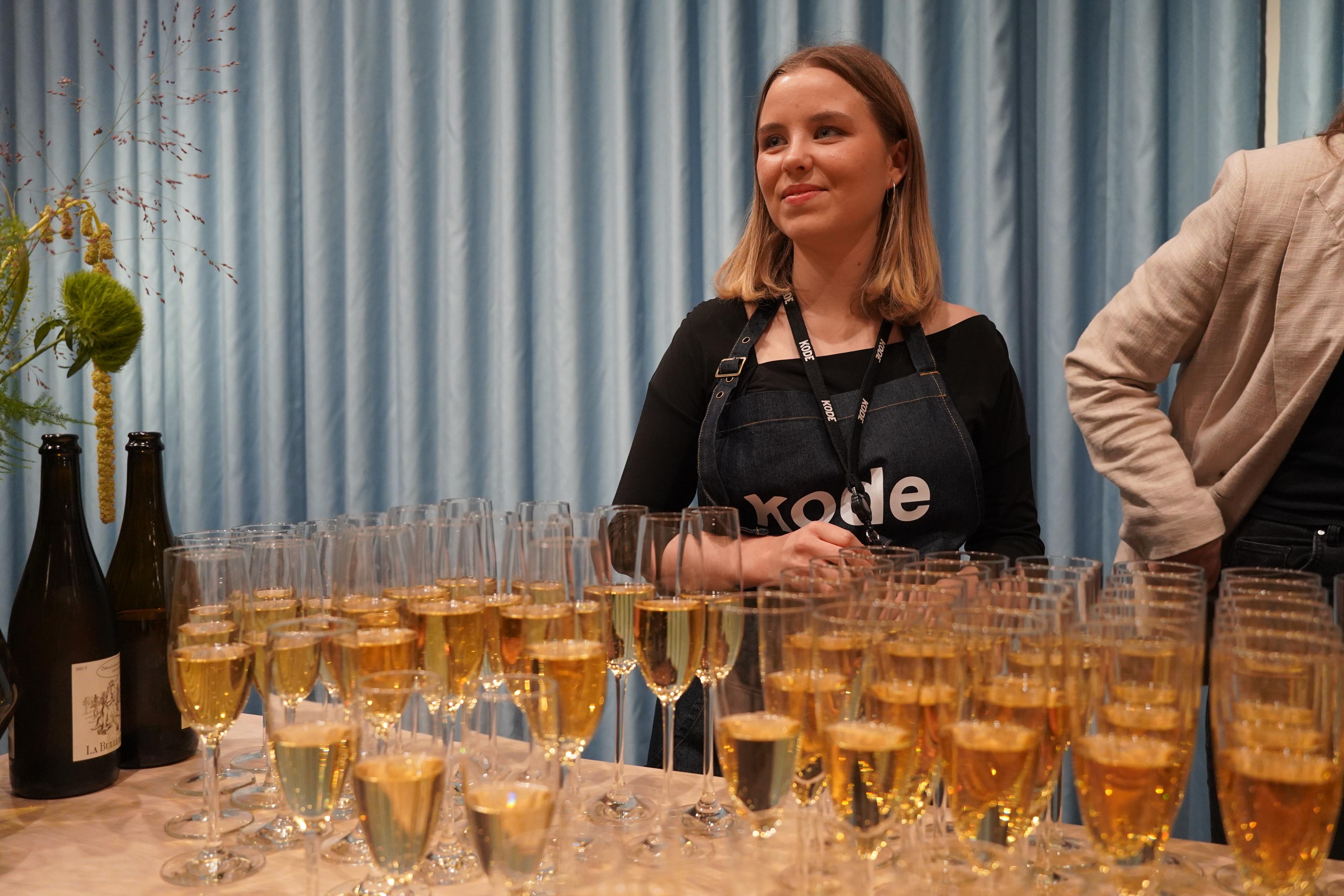 En kvinne står med Kode-forkle bak en rekke champagneglass