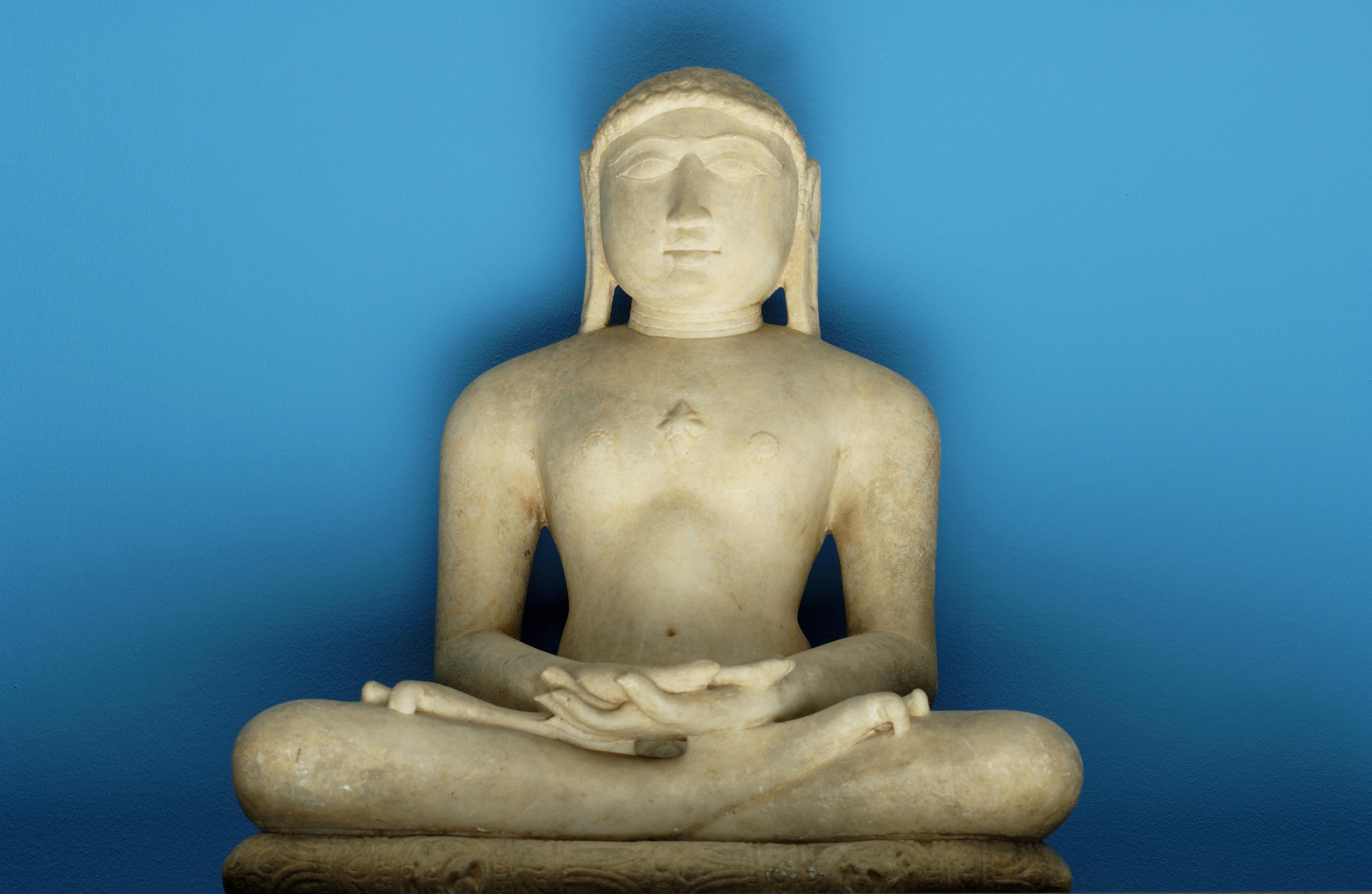 En skulptur av en helgen utført i hvit marmor, sittende med bena og armene krysset.