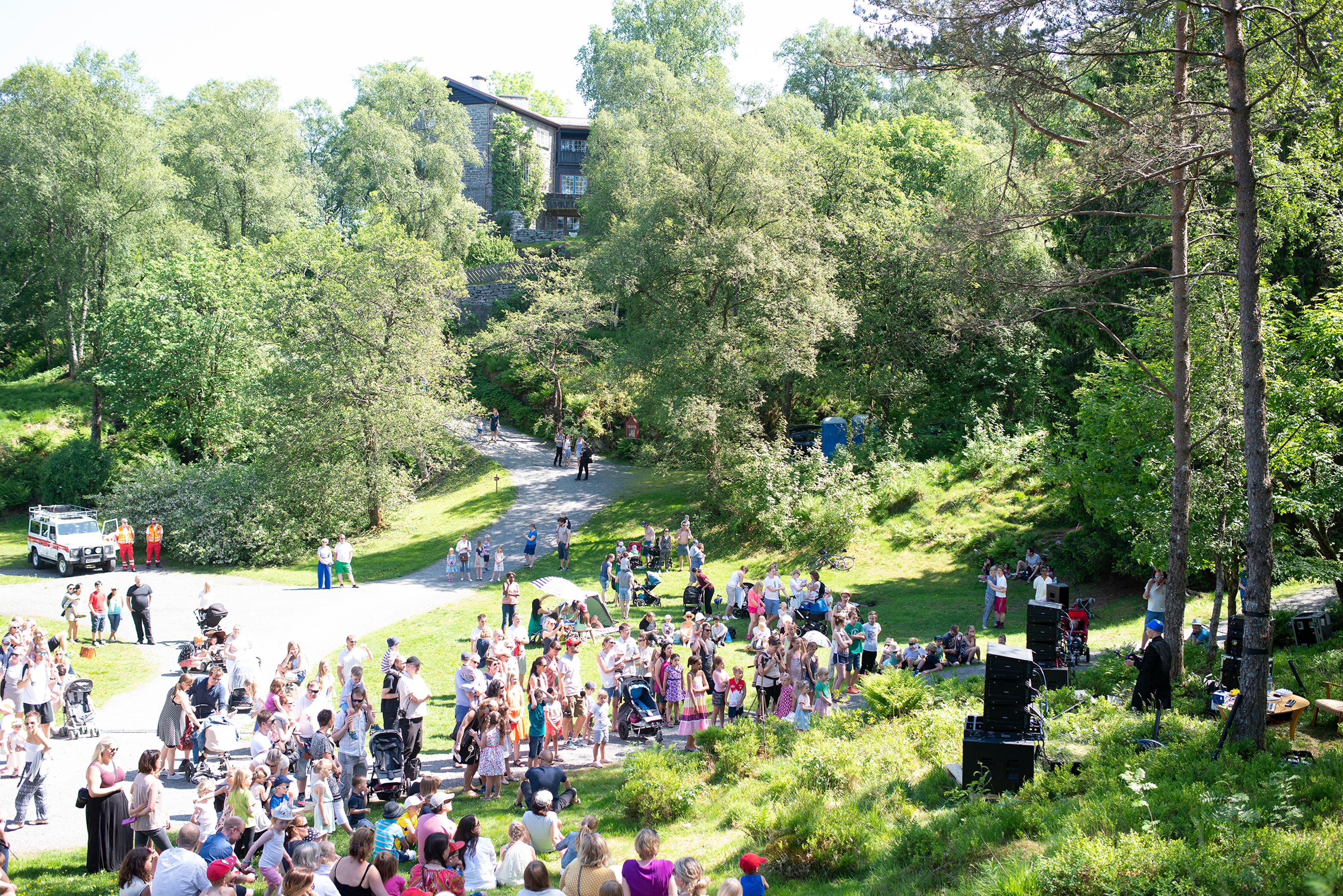 En stor gruppe mennesker på uteområdet på Siljustøl. Vi ser villaen i bakgrunnen og det er lyst sommervær.