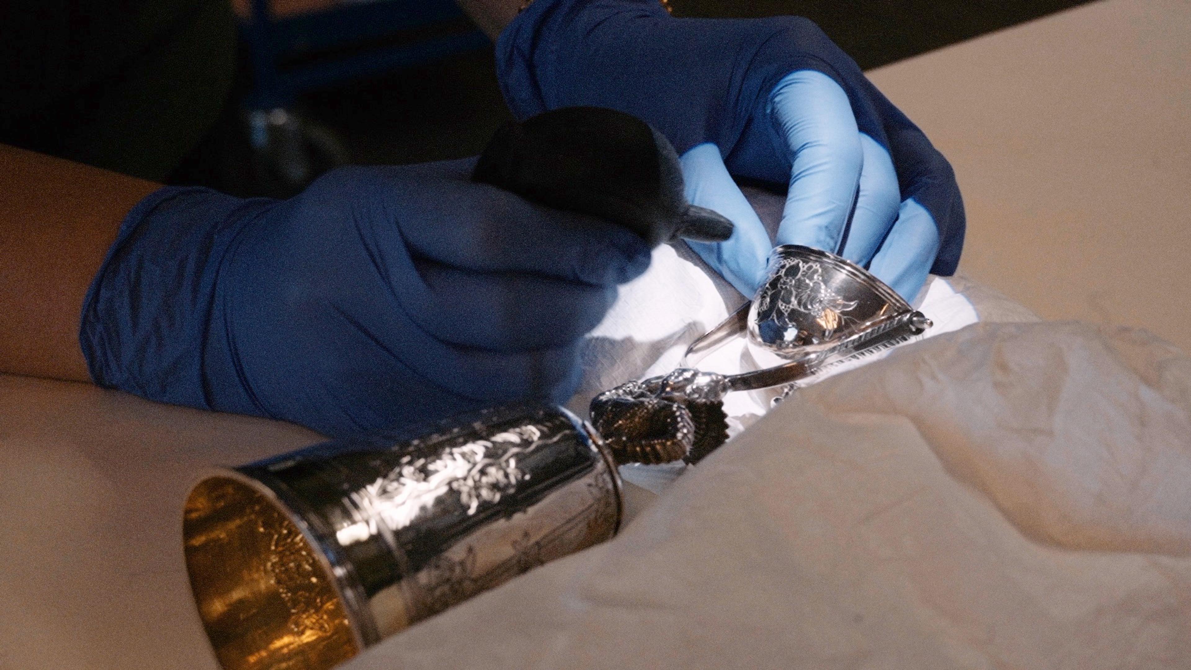 En sølvgjenstand rengjøres forsiktig av et par hender ikledd hansker