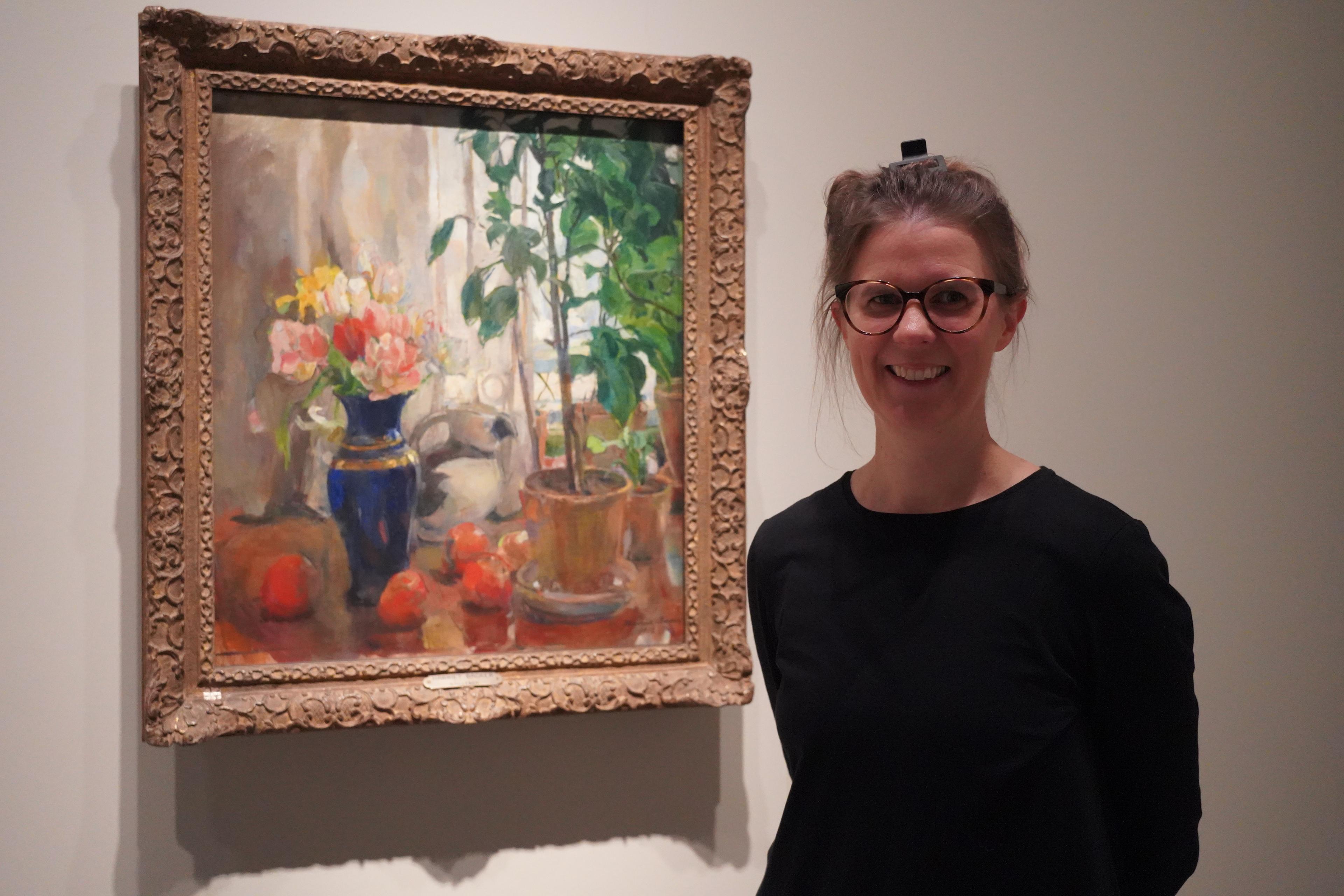 En kvinne står foran et maleri av Harriet Backer