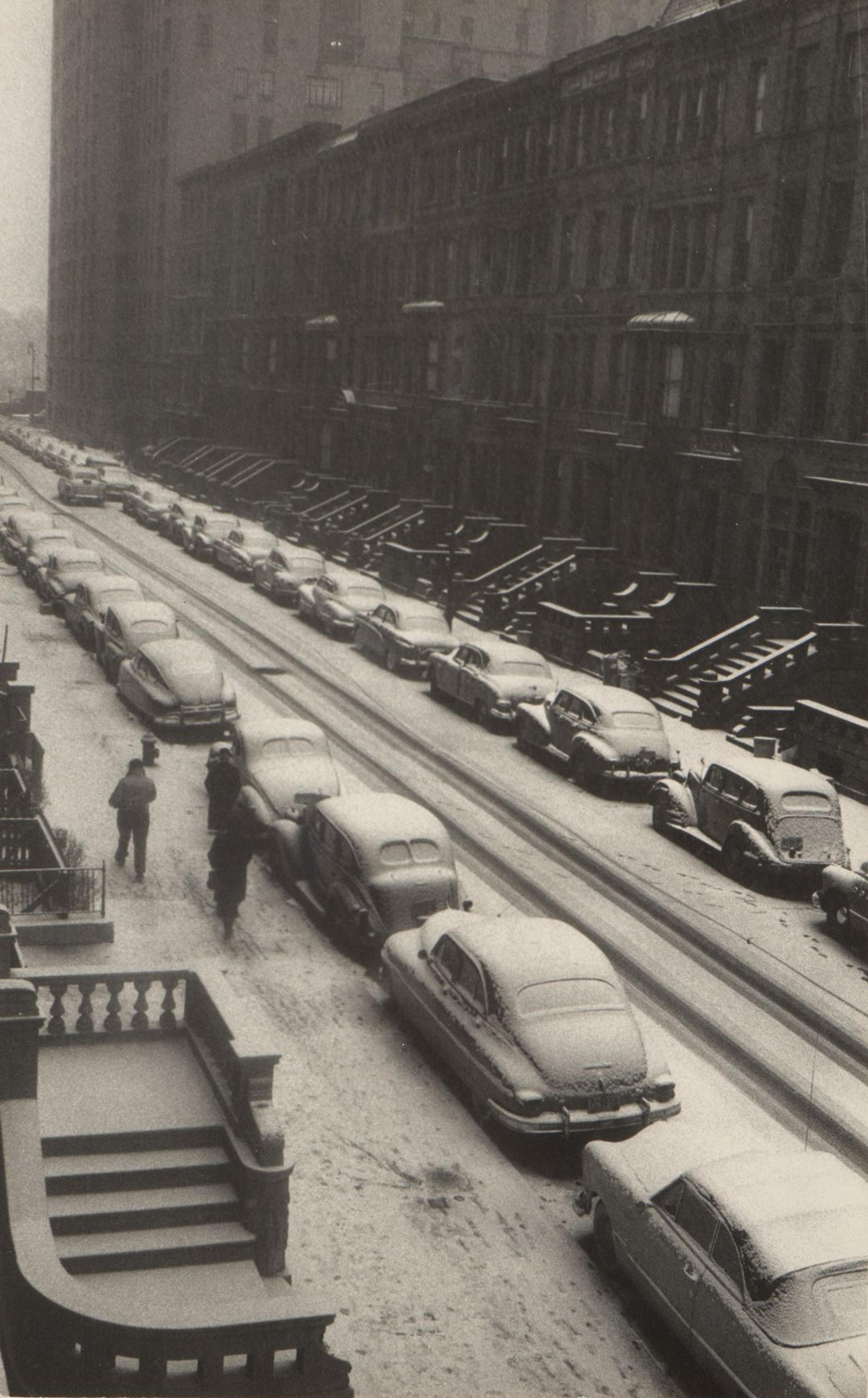 Sort-hvitt foto av en gate med biler parkert lang, med snø på bakken.
