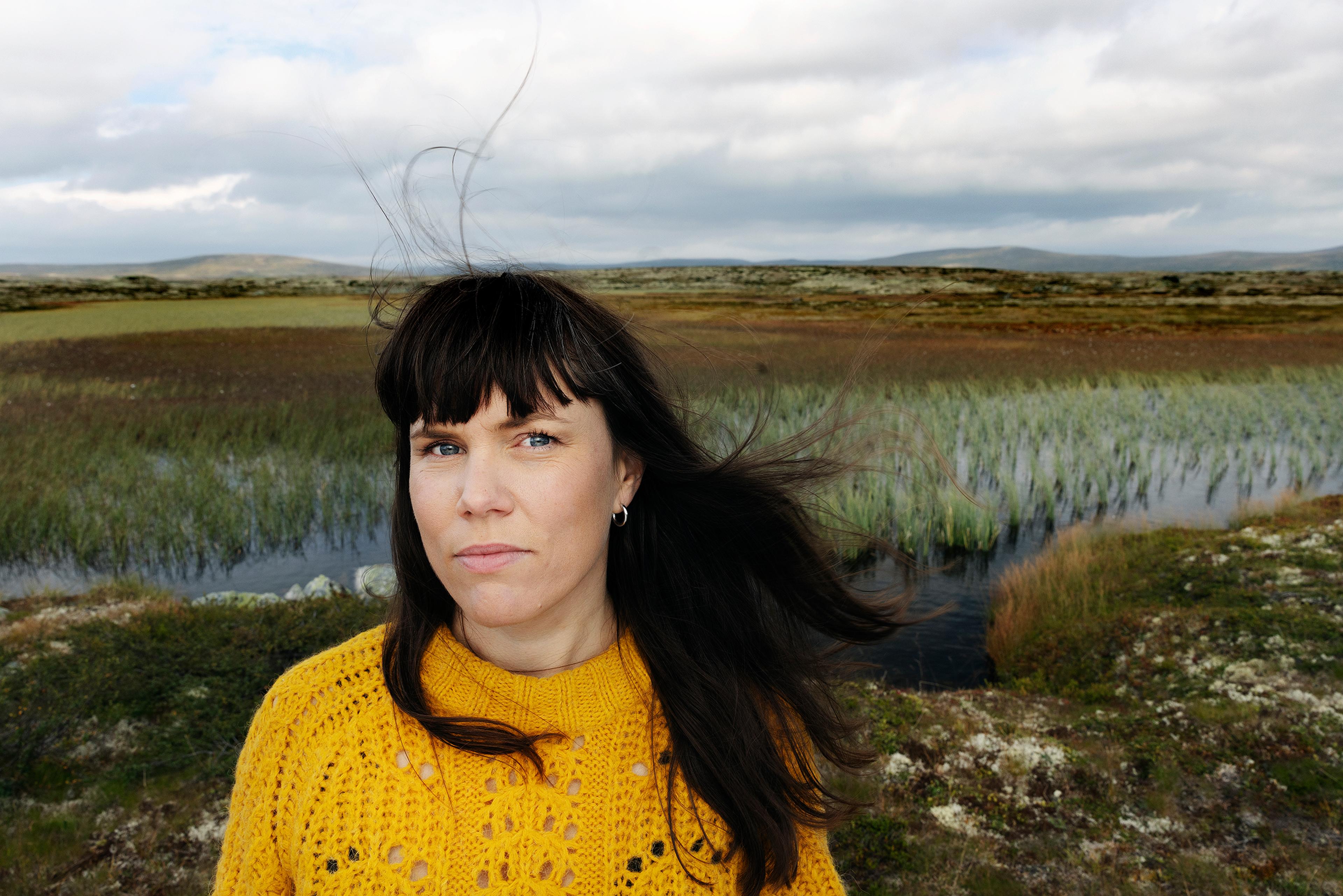 et portrett av en kvinne som står i et landskap og ser direkte mot kamera