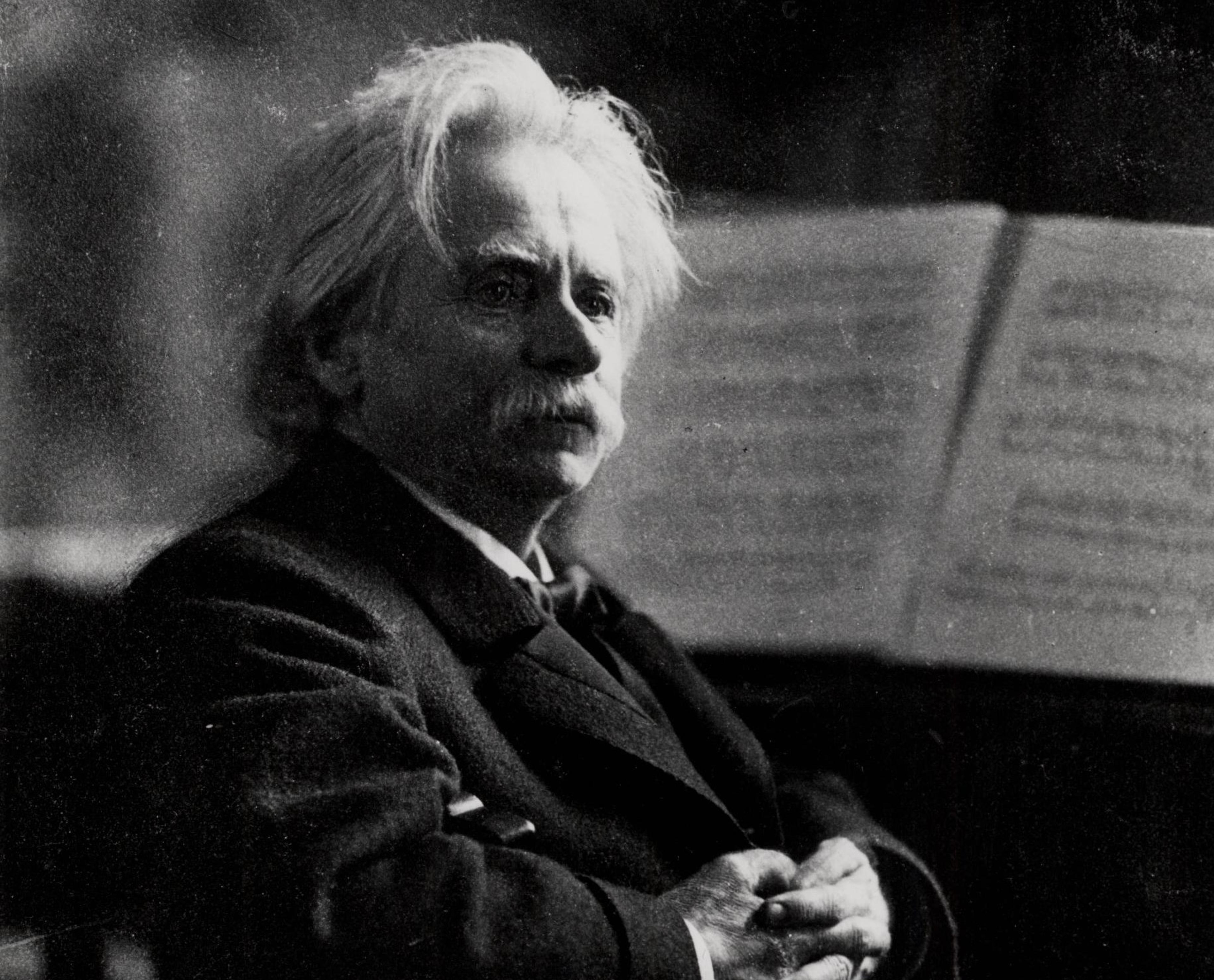 Sort-hvitt foto av Edvard Grieg. Han ser mot høyre og har armene i fold.