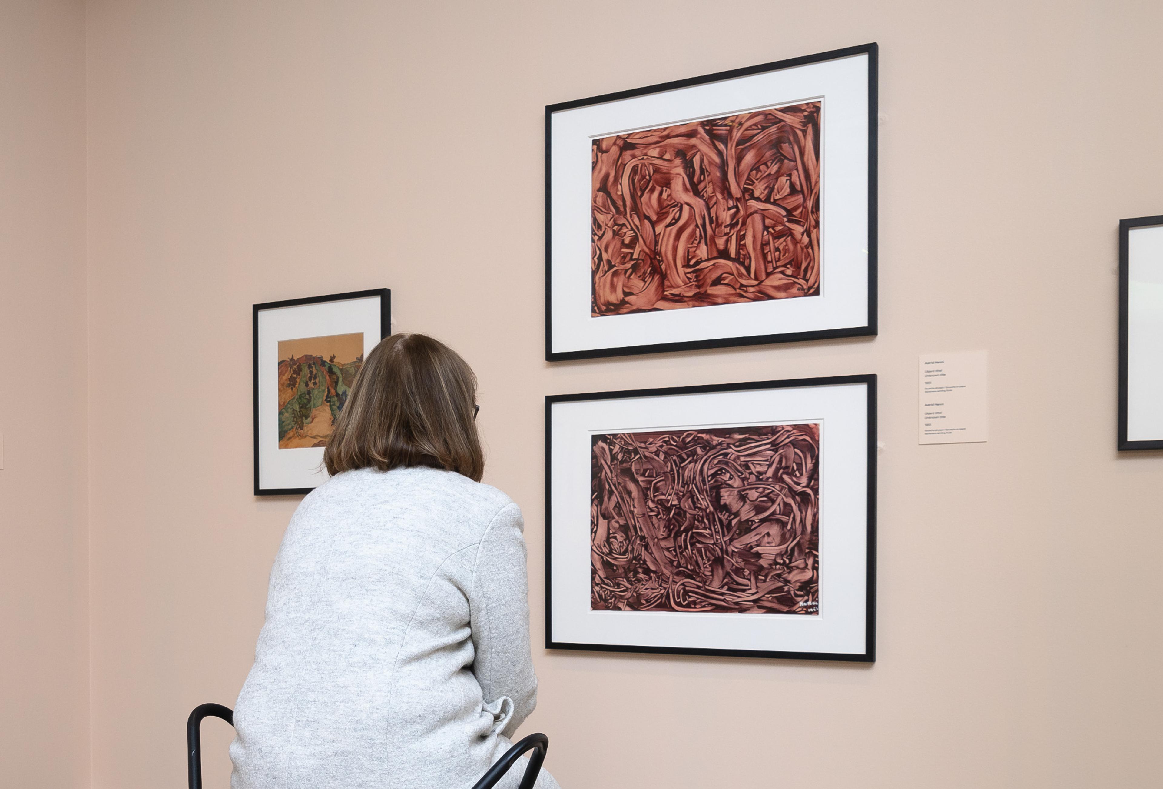 En kvinne sitter på en stol og ser på to abstrakte malerier