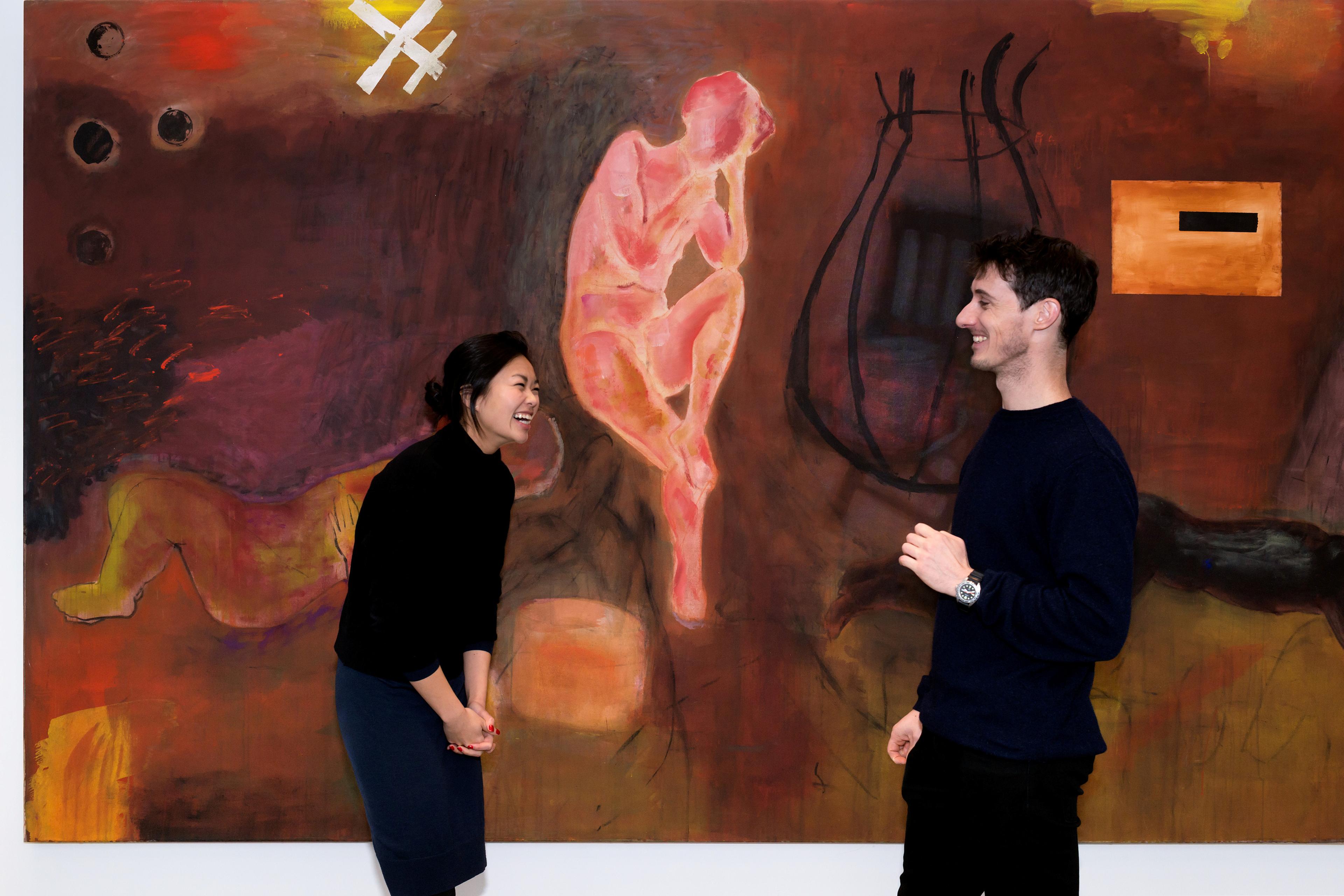 Two people standing in front of a large abstract painting. They are smiling.