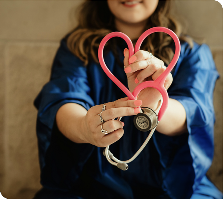 A clinician in blue scrubs shaping a pink stethoscope into a heart.