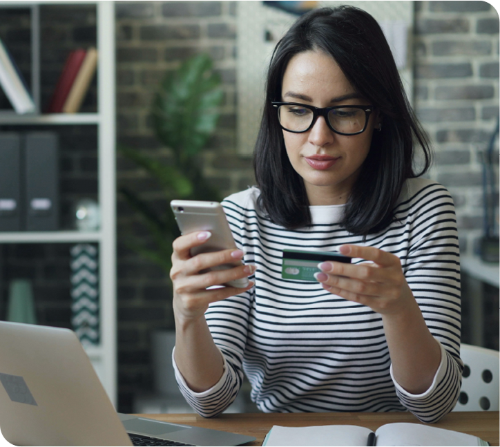 A woman at a desk entering a payment card number into her phone.