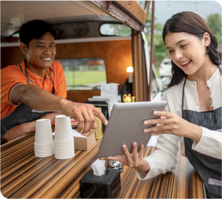 A customer at a food truck window using a tablet while the vendor points at the screen.