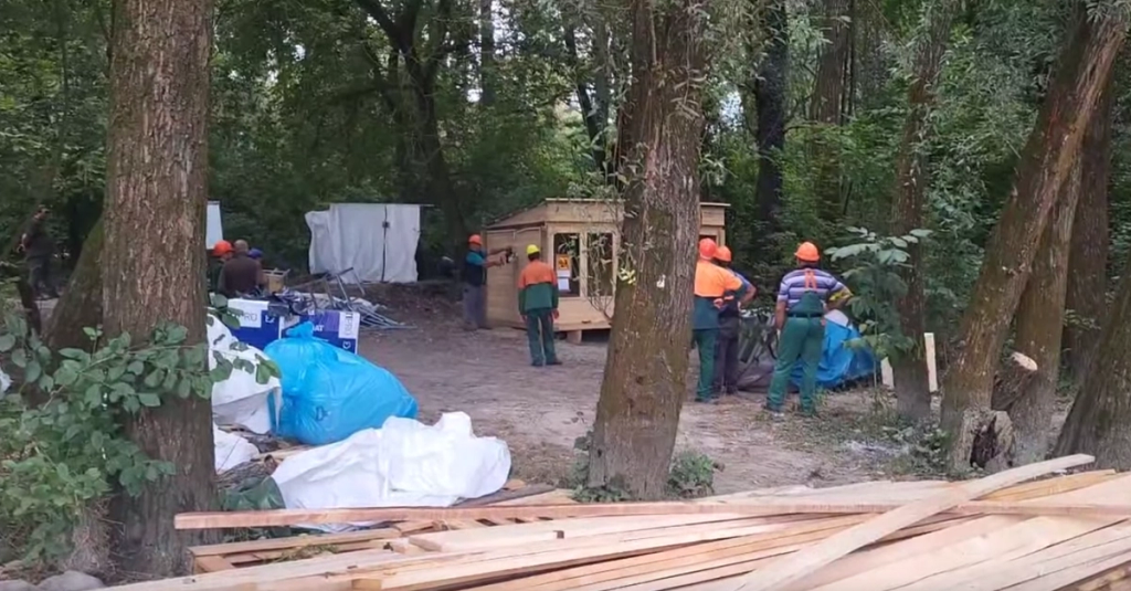 Forestry workers in orange helmets tearing down wooden houses in the Liberland forest, September 2023
