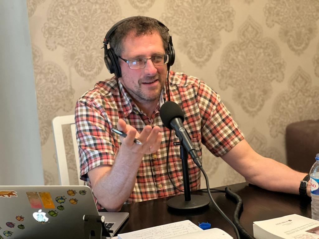 Man in headphones speaking into a microphone during a Free Cities Podcast recording at Zuzalu