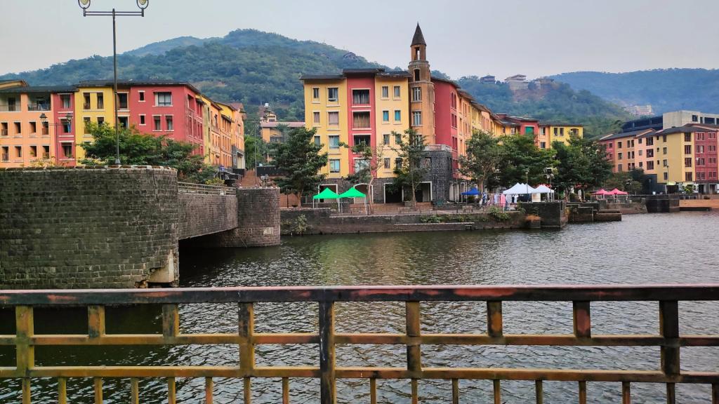 Colourful waterfront buildings and a clock tower on the lake in Lavasa, seen from a bridge railing