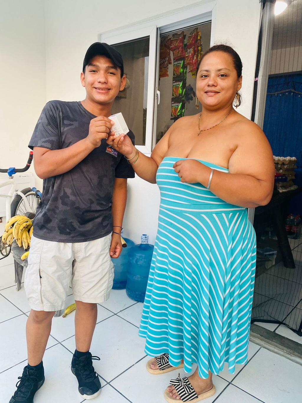 Anthoni handing a prize to a smiling woman outside a minimarket in Ciudad Morazán, Honduras