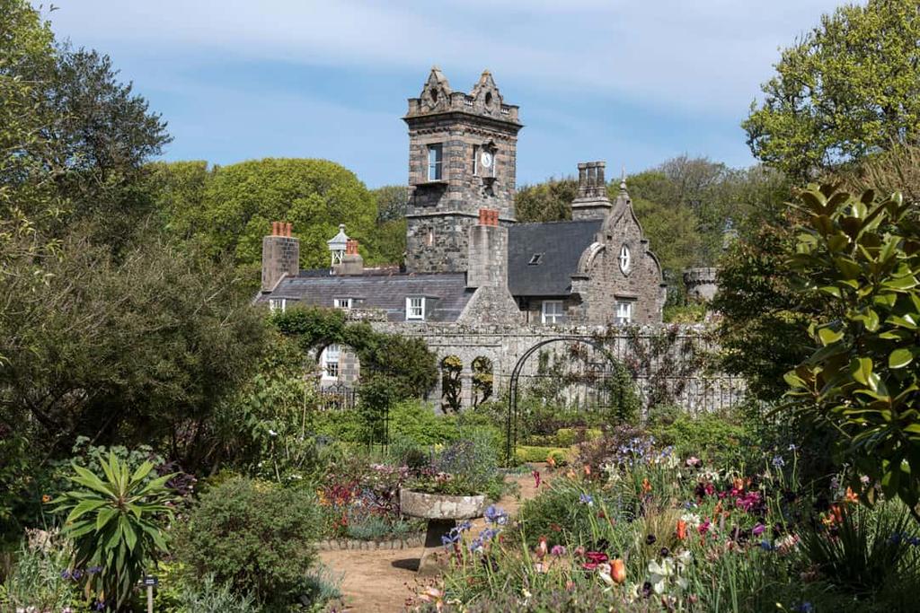 Flower garden in front of a granite manor house with a tower on Sark
