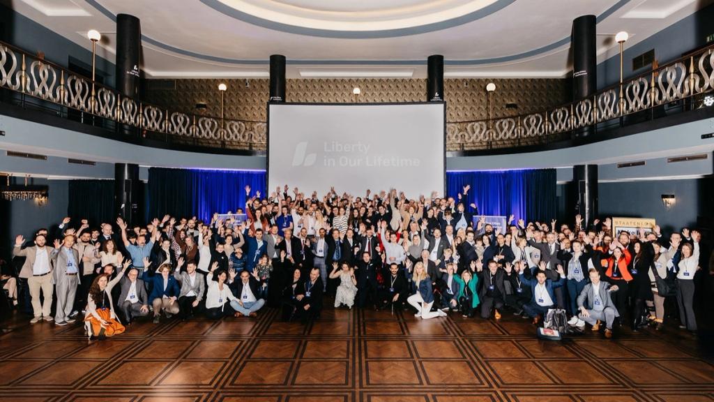 Attendees waving in the group photo of the Liberty in Our Lifetime Conference 2024 in a grand ballroom