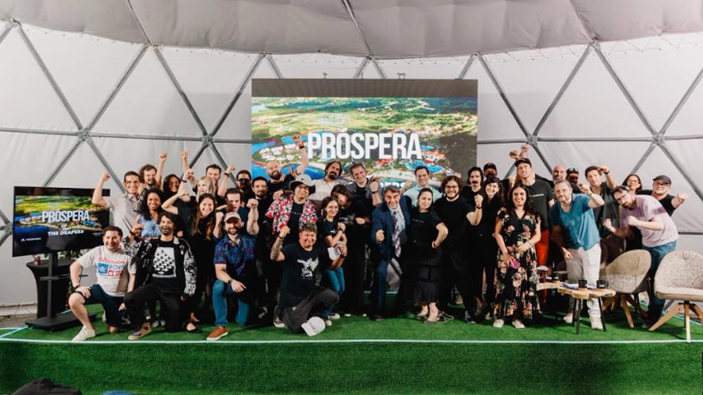 Large group cheering in a geodesic dome in front of a screen reading Próspera