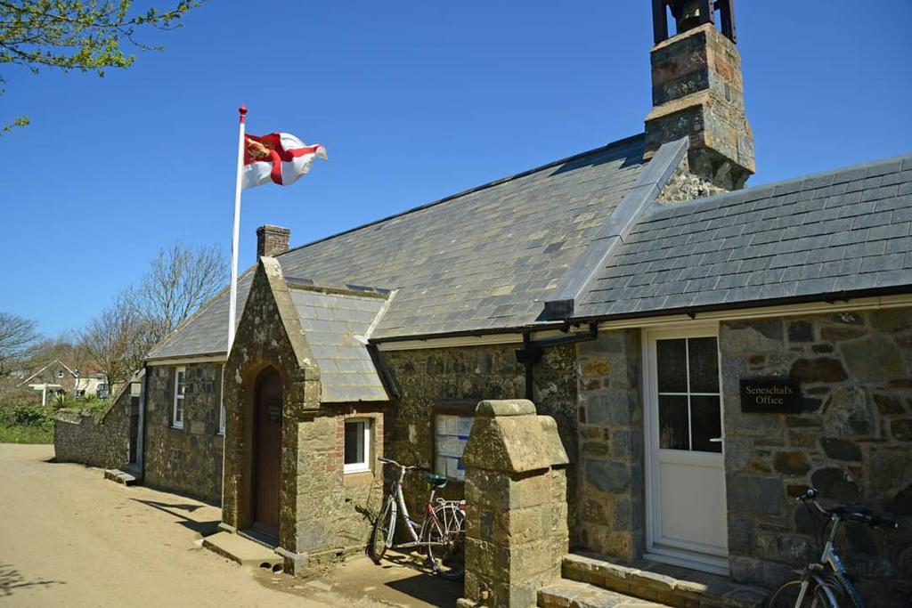 Granite cottage with slate roof and the Sark flag beside a quiet lane