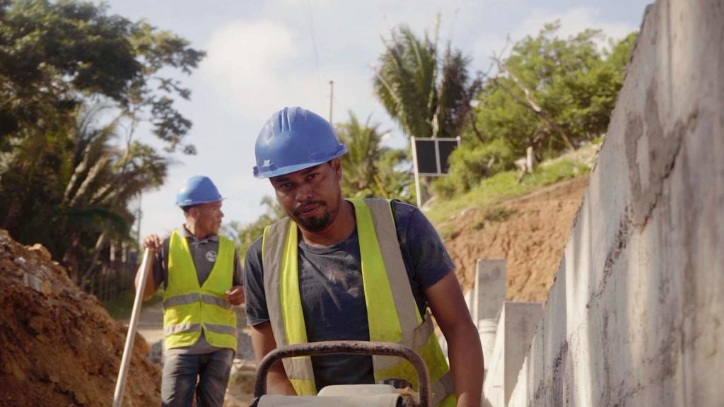 Trabalhadores de capacete azul e colete refletivo em um canteiro de obras em Roatán Próspera