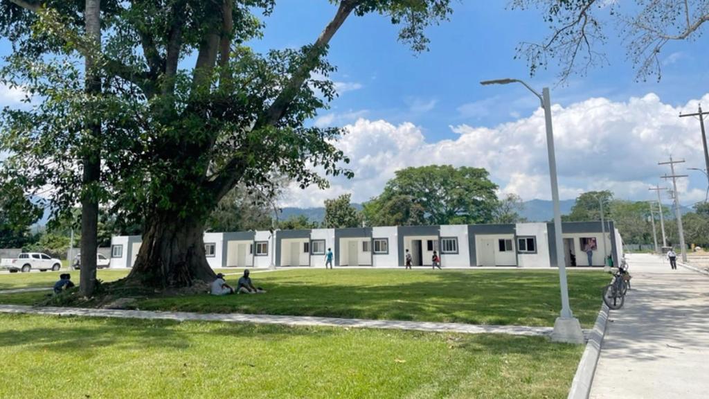 Row of single-storey apartment blocks beside a lawn and large tree in Ciudad Morazán, Honduras