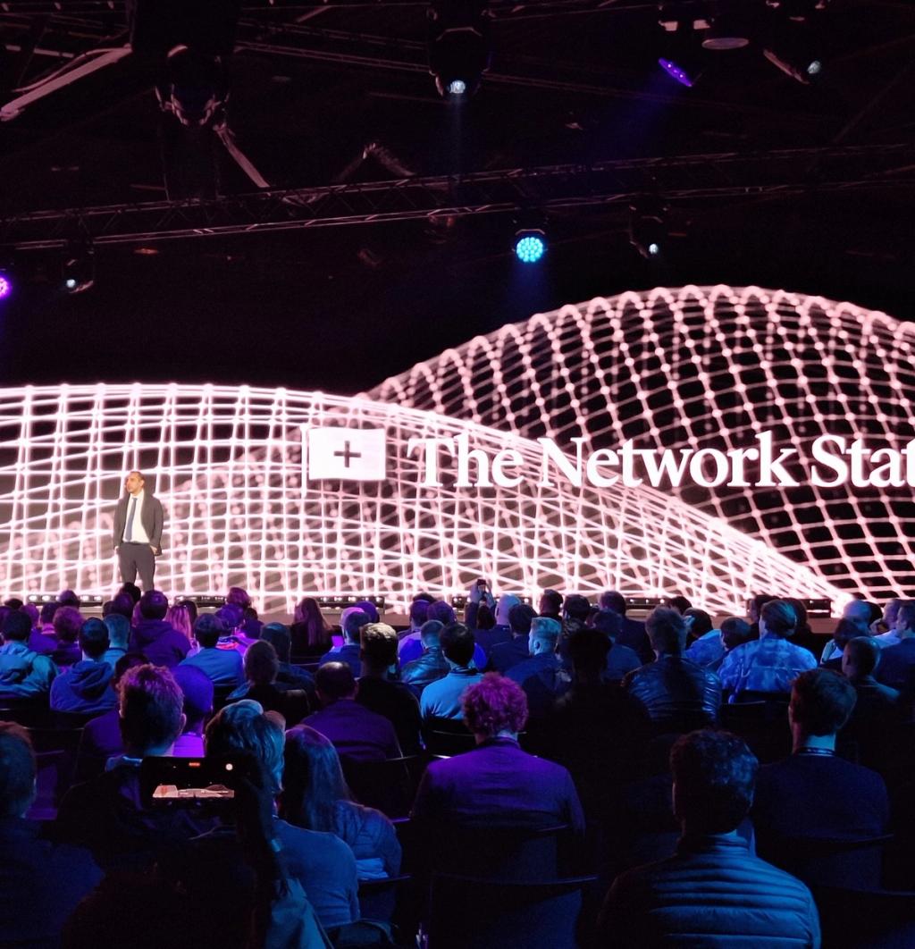 Balaji Srinivasan opening the Network State Conference in Amsterdam before a glowing mesh backdrop and packed audience