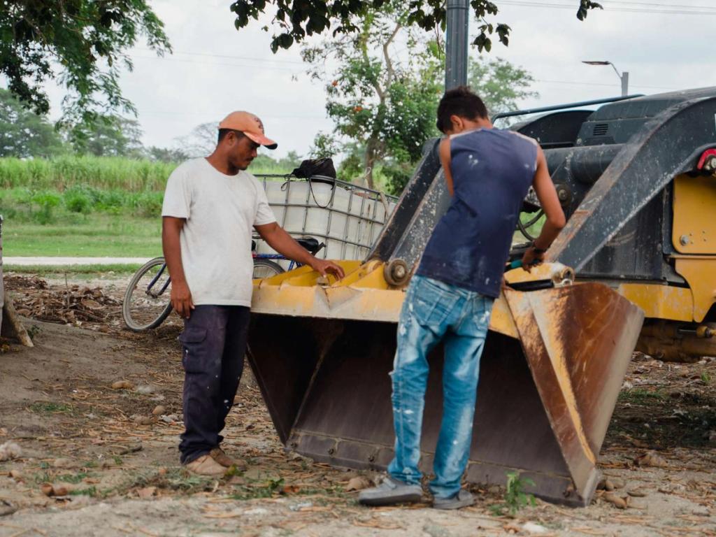 Construction workers beside a yellow loader bucket in Ciudad Morazán, Honduras