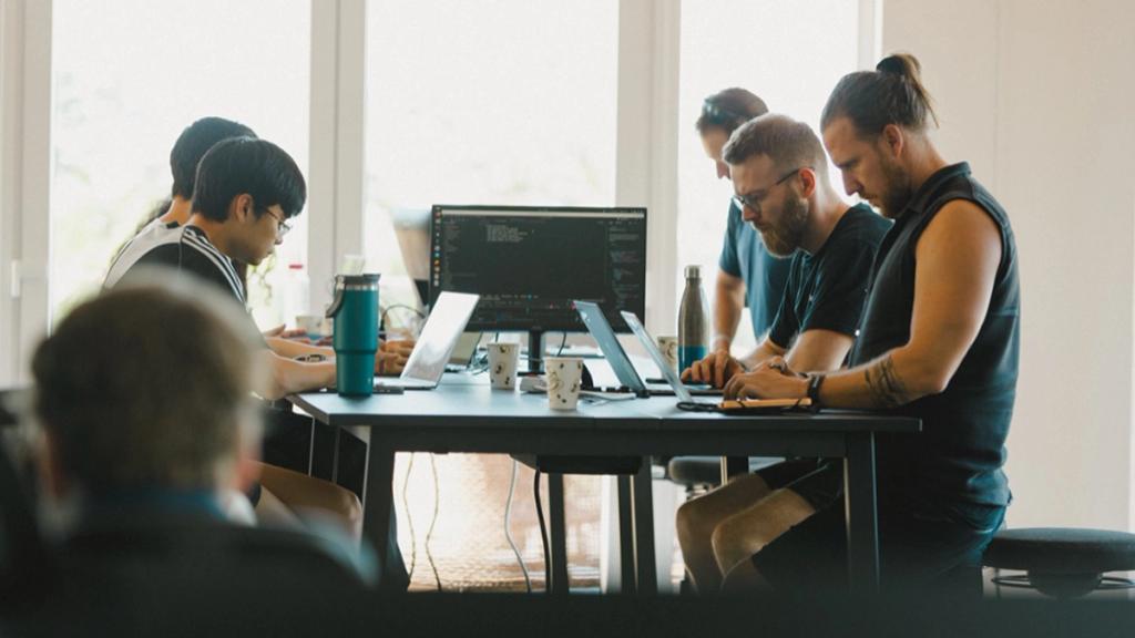 Próspera residents working on laptops at a shared desk in the Duna Tower co-working space