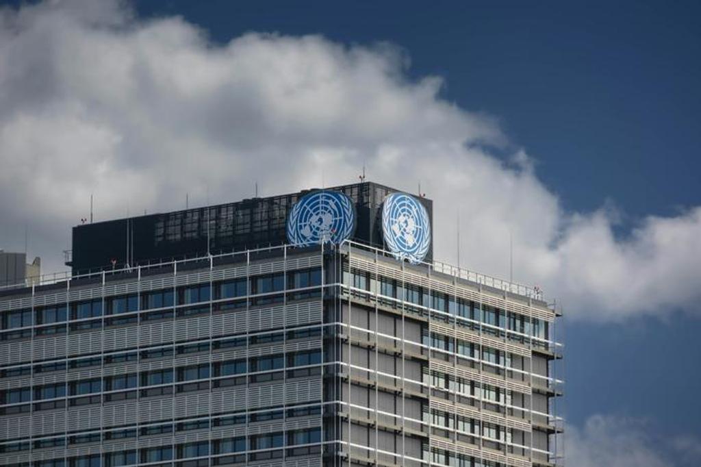 Office tower topped with United Nations emblems against a cloudy blue sky