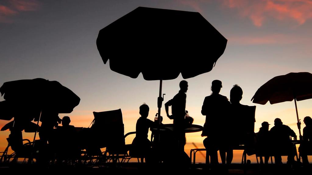 Silhouettes of Gran Pacifica residents gathered under beach umbrellas at sunset