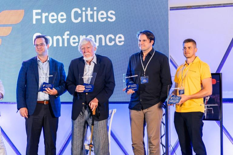 Erick Brimen, Oliver W. Porter, Niklas Anzinger and Danny Hertle holding their awards on stage at the Free Cities Conference 2026 in Próspera