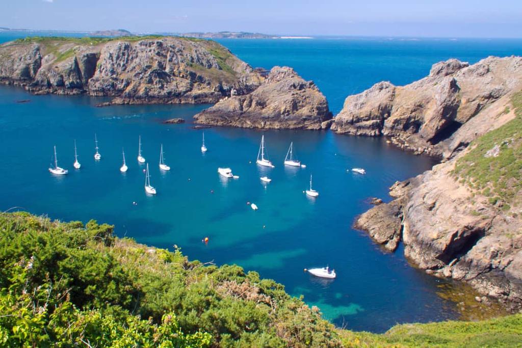 Sailing yachts anchored in a turquoise bay below rocky cliffs on the island of Sark