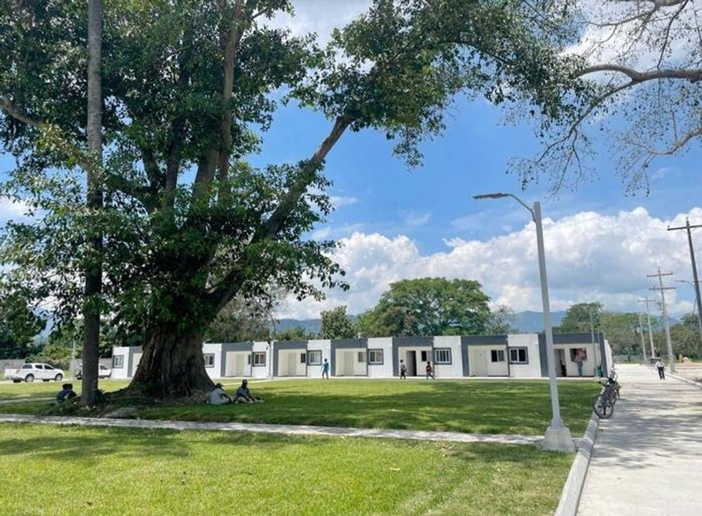 Row of new single-storey homes behind a large shade tree and lawn in Ciudad Morazán, Honduras